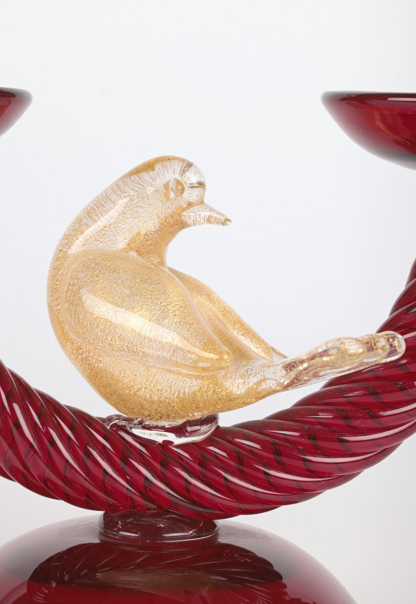 An unusual and stunning Italian Venetian mid-century ruby glass bird mounted twin candlestick made on Murano. The candlestick is of simple form raised on a simple round domed base with a thick U formed twisted glass rod supporting two candle holders