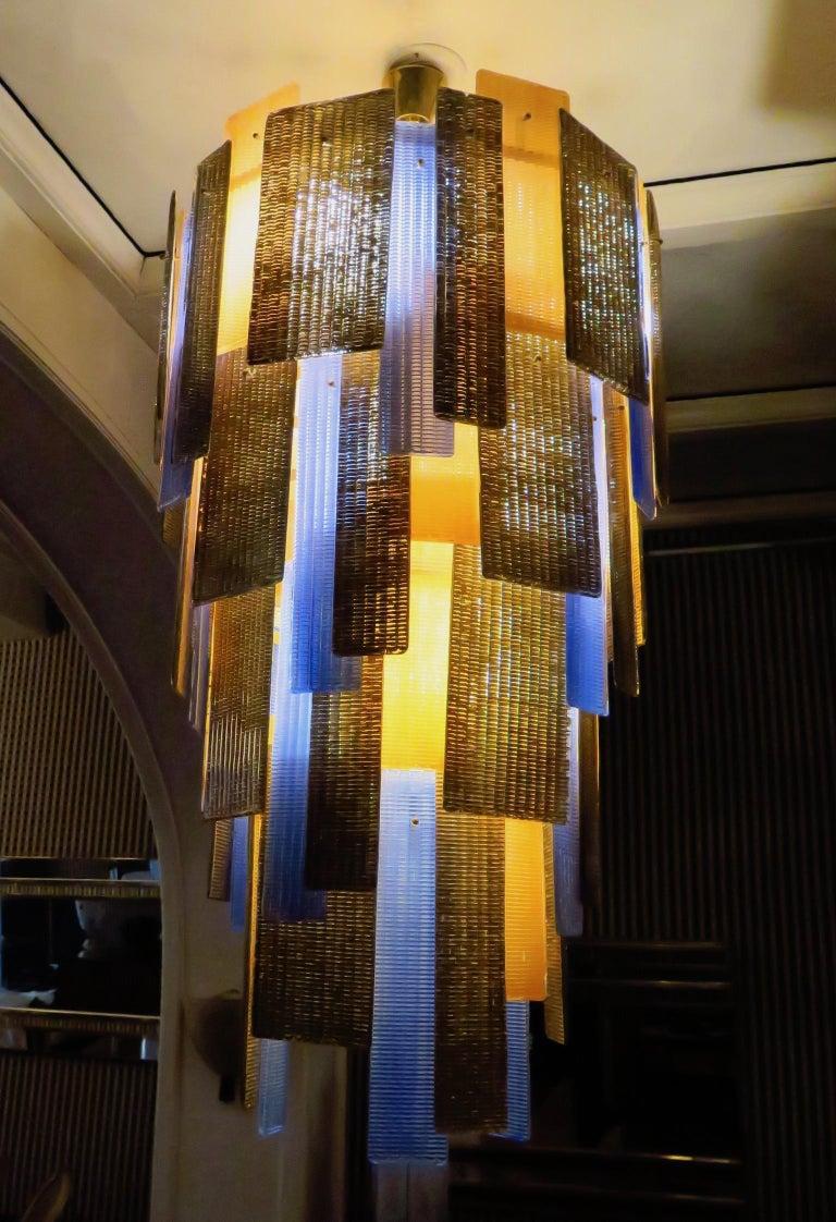 Murano midcentury art glass Chandeliers, with a very special color.

White lacquered iron structure. All around are big and small colored Murano glass tiles hanging. The colors are gold, light pink and blue. The chandelier is round in shape and