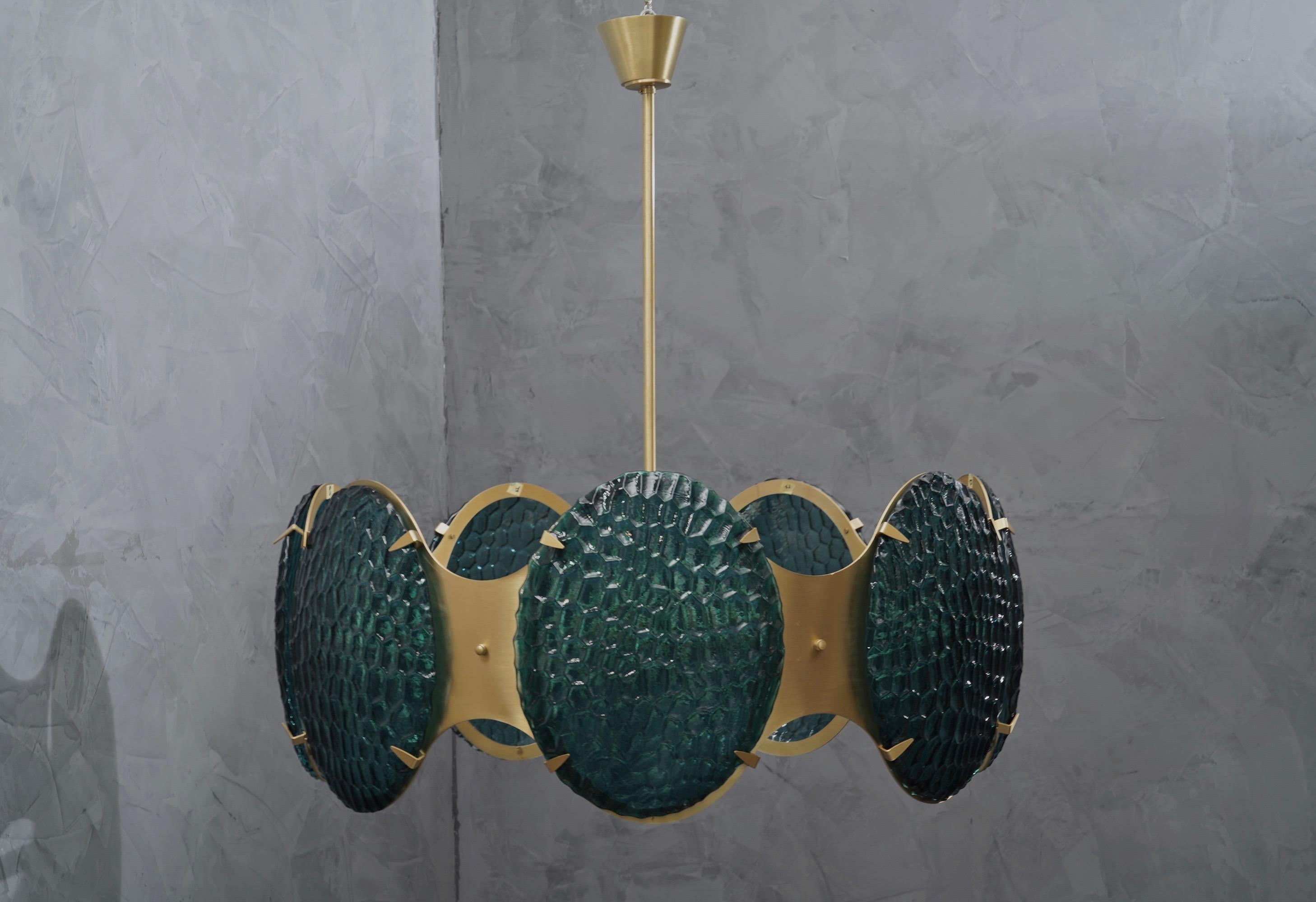 A fascinating round-shaped chandelier, like a giant bracelet hanging from the ceiling, large Murano glass shields act as precious stones; made with materials that blend beautifully together.

Its structure is in satin brass, has a round shape,