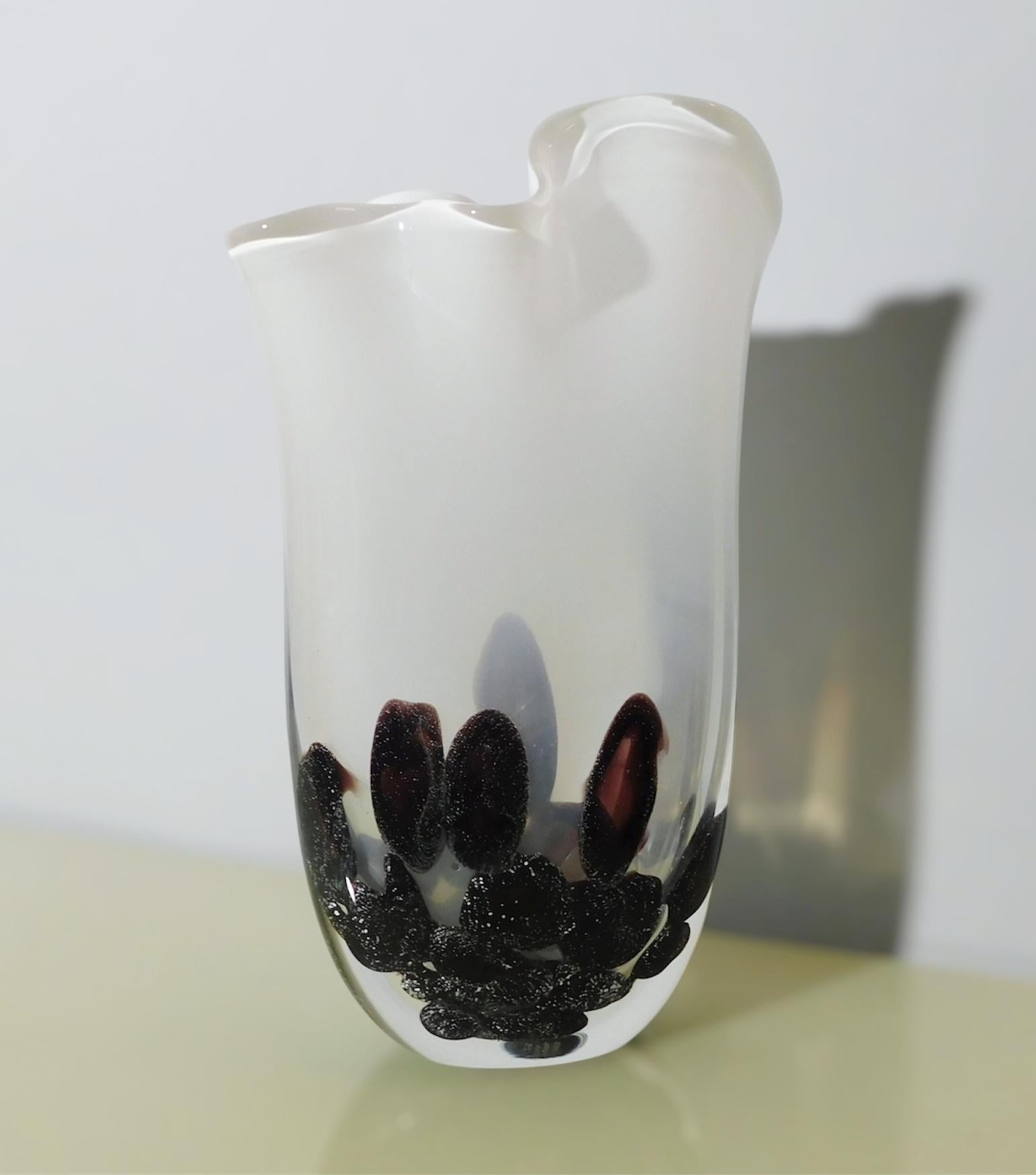 Vase aus italienischem Murano-Kunstglas mit milchig-weißem Deckel und klarem Boden, geblasen mit schwarzen Tröpfchen, die an verschiedene Kieselsteine erinnern / Hergestellt in Italien von Lorenzo Povolato, um 1990
Original Herstellermarke auf der