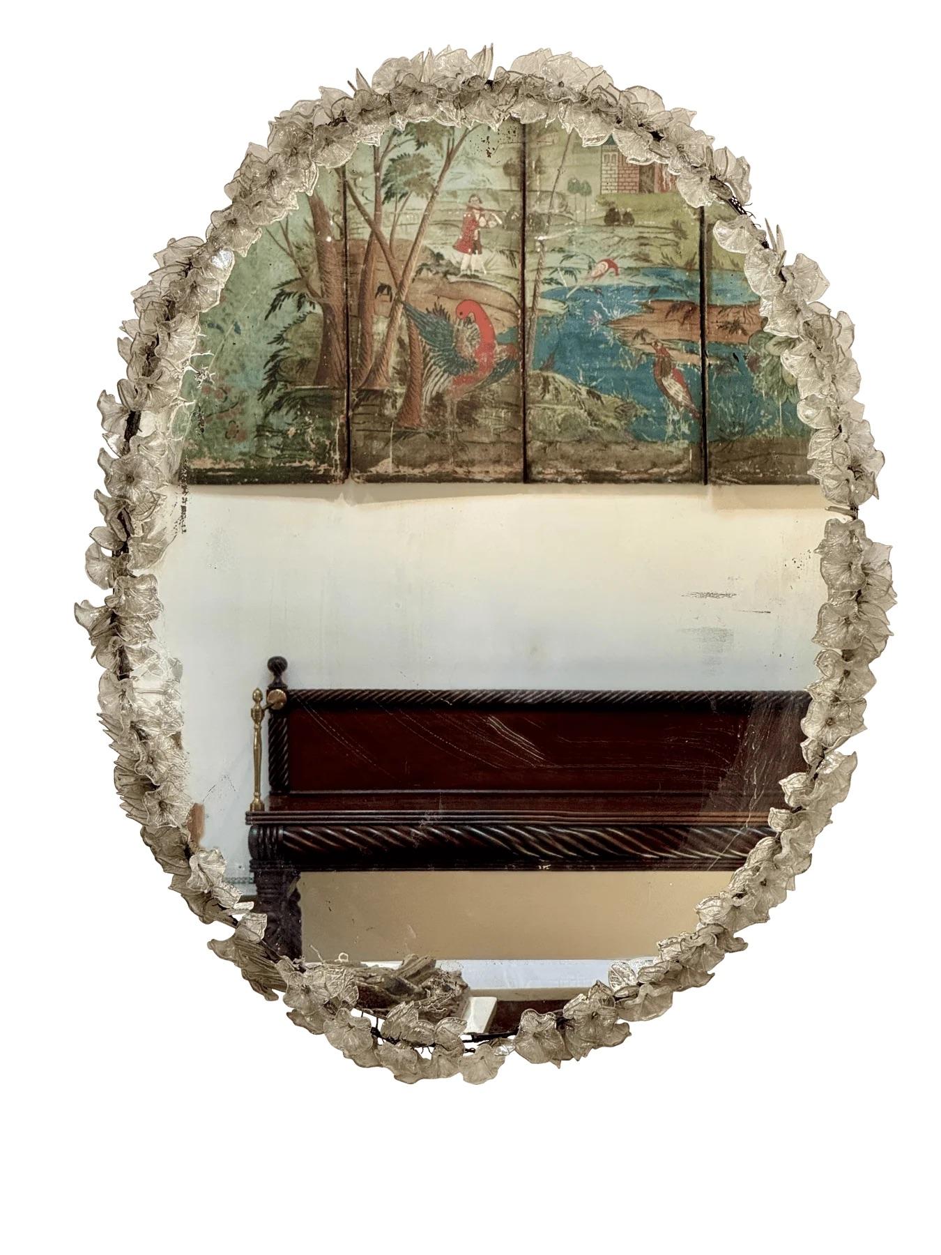 Ce miroir mural ovale est encadré de fleurs en verre de Murano soufflées à la main. Chaque fleur présente de fines nervures et de subtiles mouchetures d'or, caractéristiques de l'art vénitien du milieu du 20e siècle. Probablement fabriqués sur l'île
