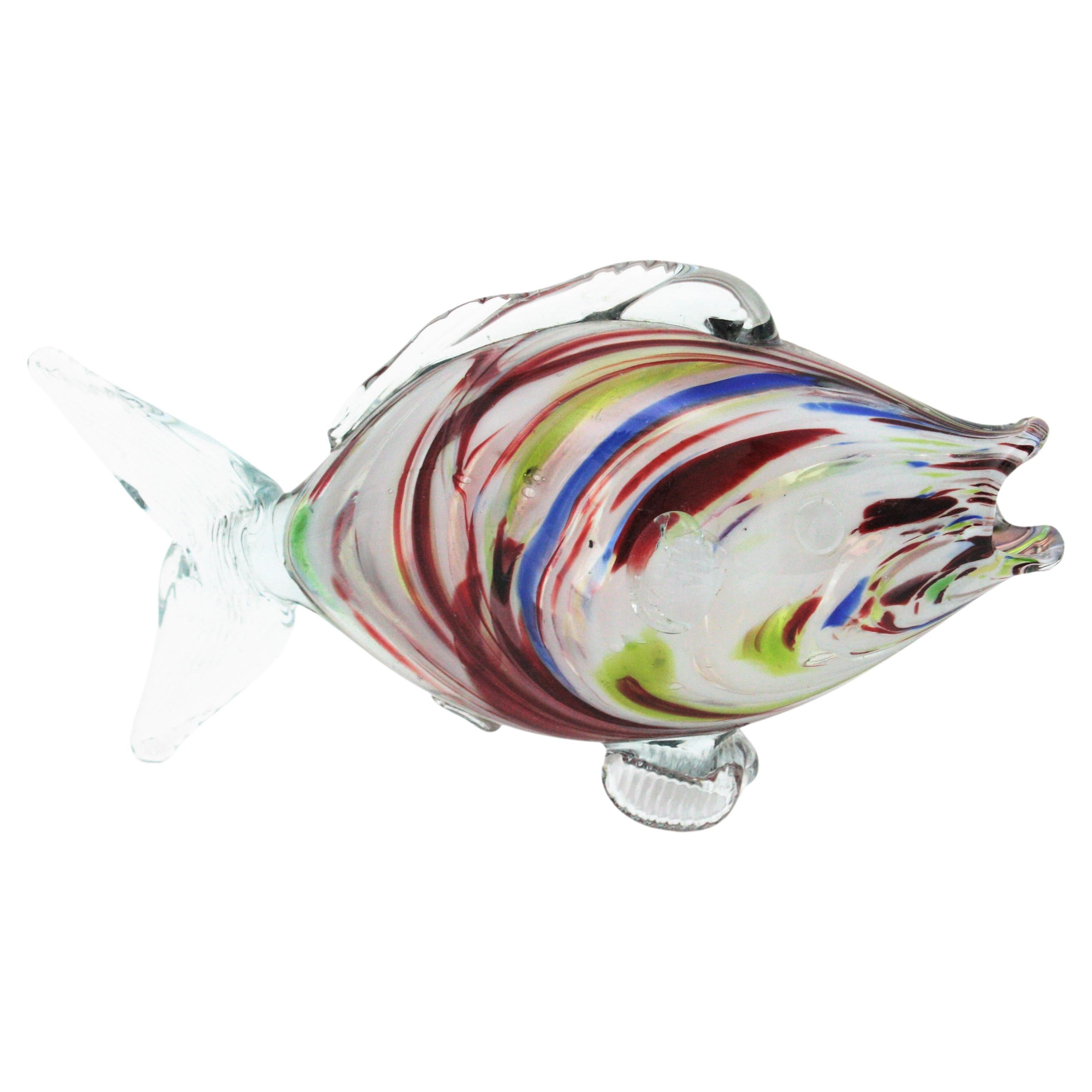 Figura di pesce in vetro di Murano soffiato a mano della metà del secolo scorso con corpo in vetro trasparente e strisce nei colori rosso e bianco e accenti in blu e verde.
Italia anni '50. 
Ogni lato del corpo ha un design diverso.
Misure: 24 cm