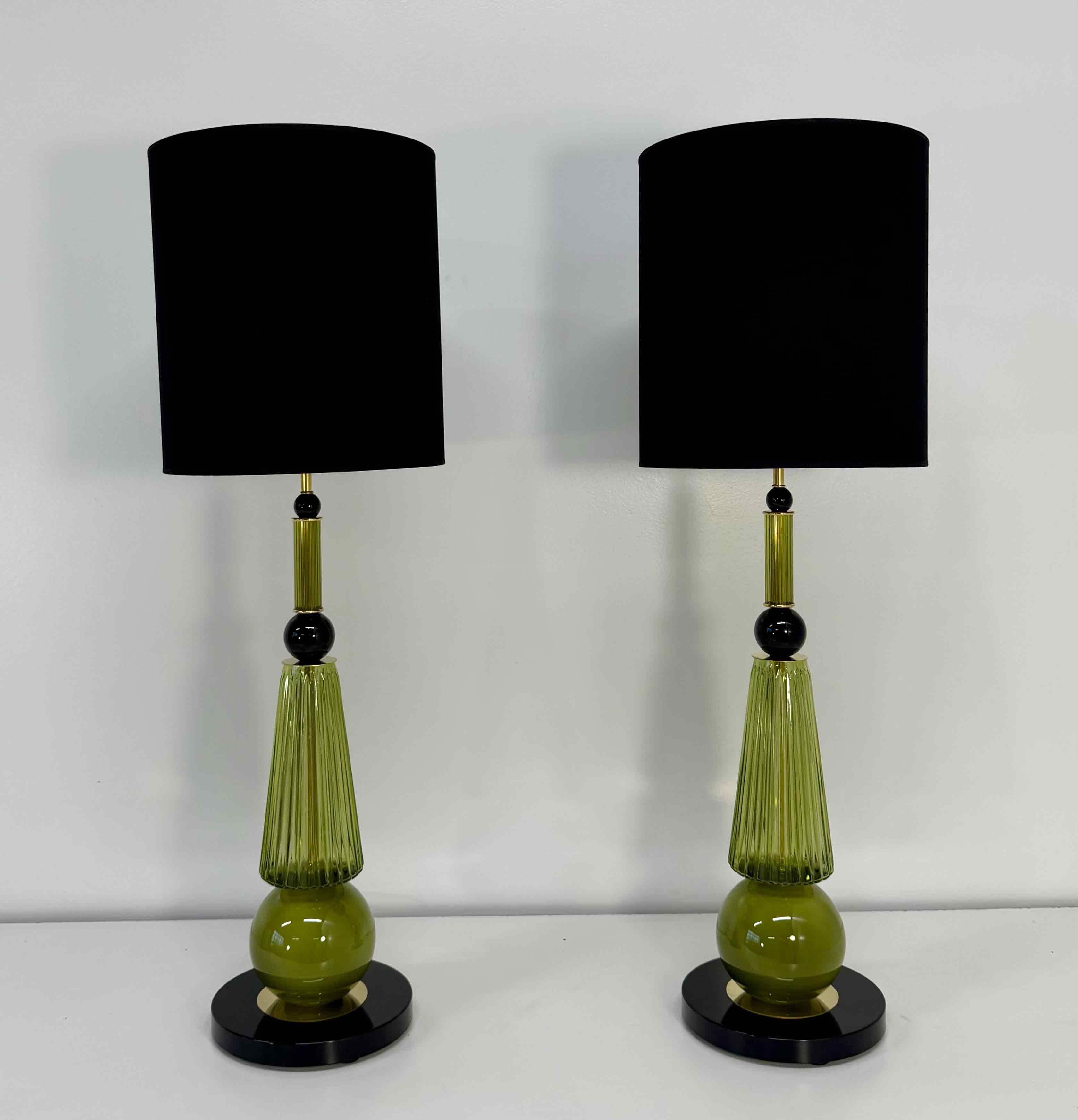 Elegante par de lámparas de mesa de cristal de Murano fabricadas a mano en Italia en la década de 2000.
Cada lámpara presenta una base de cristal verde oliva compuesta por un elemento esférico brillante y una sección central estriada soplada a mano,