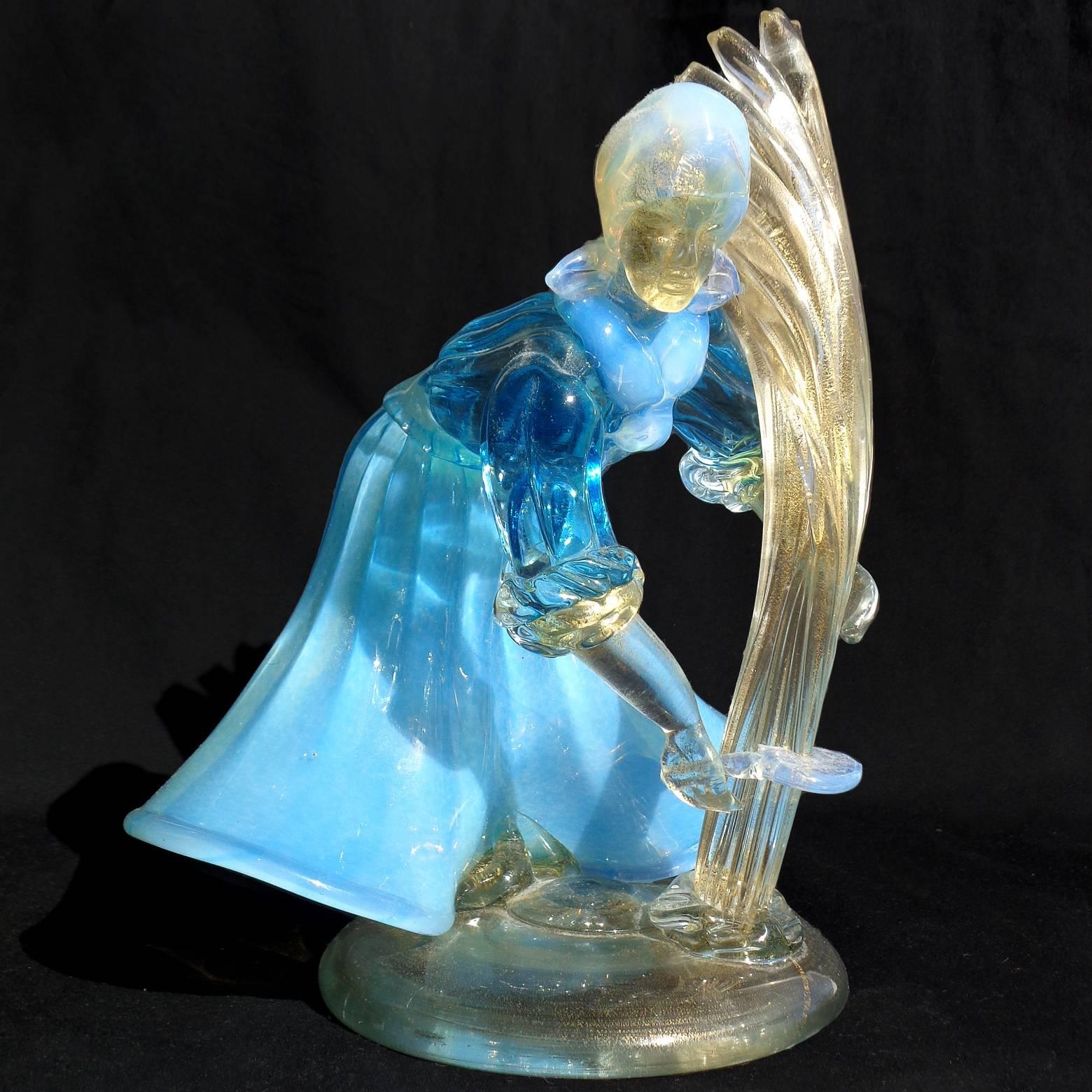 Magnifique verre d'art italien de Murano soufflé à la main, bleu et blanc opalescent, avec des mouchetures dorées, représentant une femme fermière. Attribué à la société A.Ve.M. (Arte Vetraria Muranese). La femme est en action, elle coupe sa