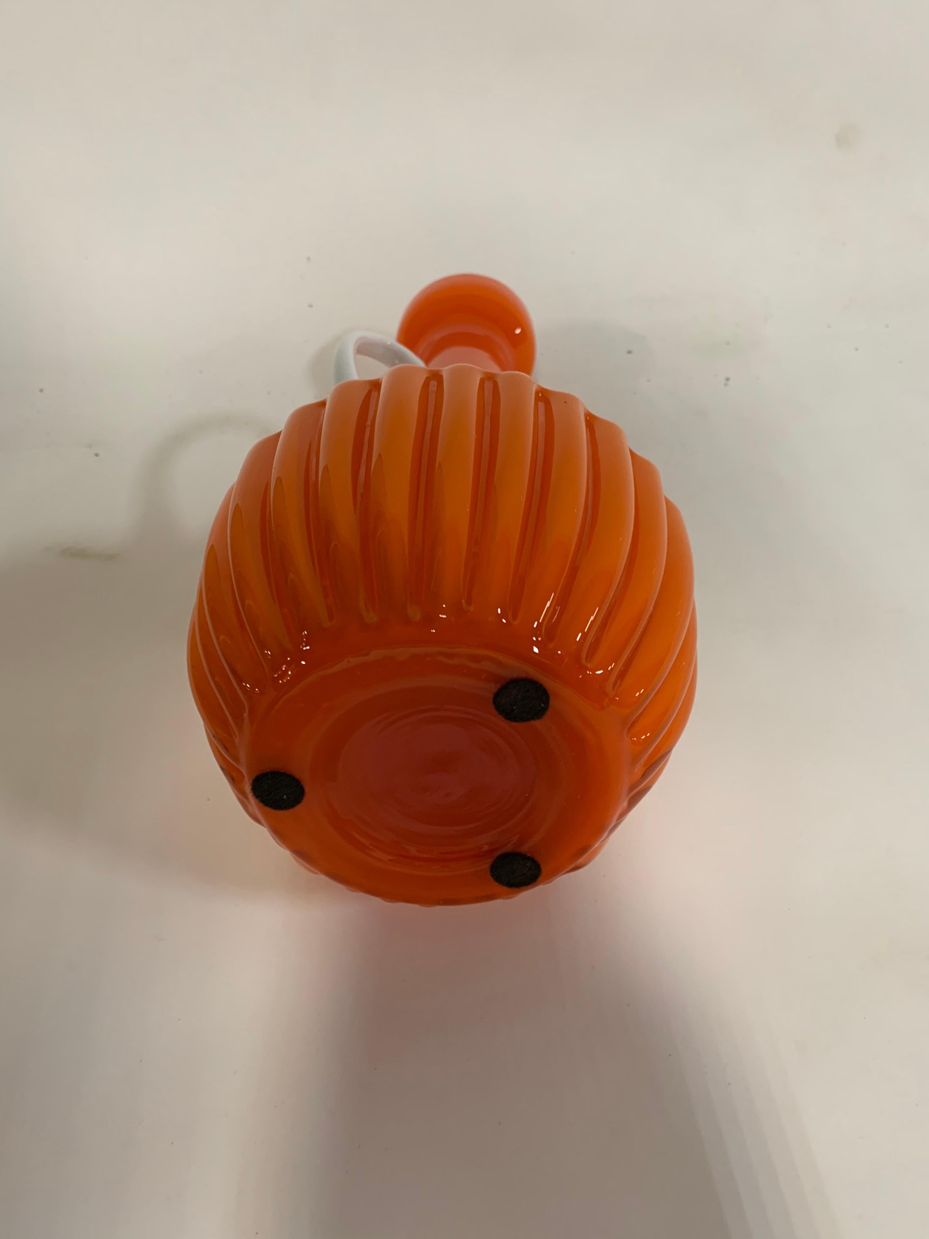 Un vaso con manico in vetro di colore arancione e bianco.

Italia, circa 1960.  Senza segno.

Dimensioni:
13