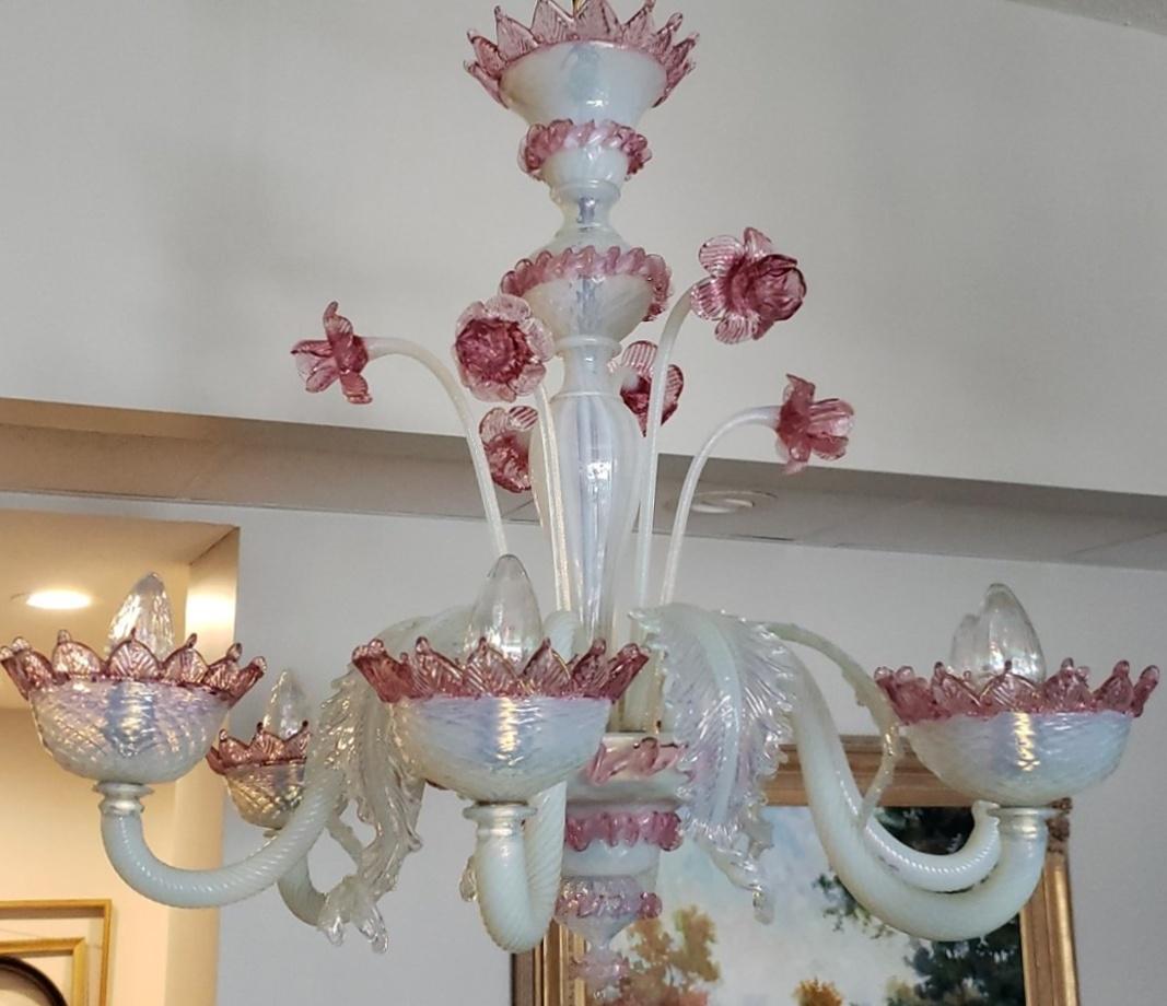 Fabriqué avec précision, ce lustre Murano d'Italie présente un verre opalin d'une délicate teinte rose, formant six bras en S ornés de fleurs vers le haut et de feuilles vers le bas. La combinaison du verre opalin, des accents roses et du motif