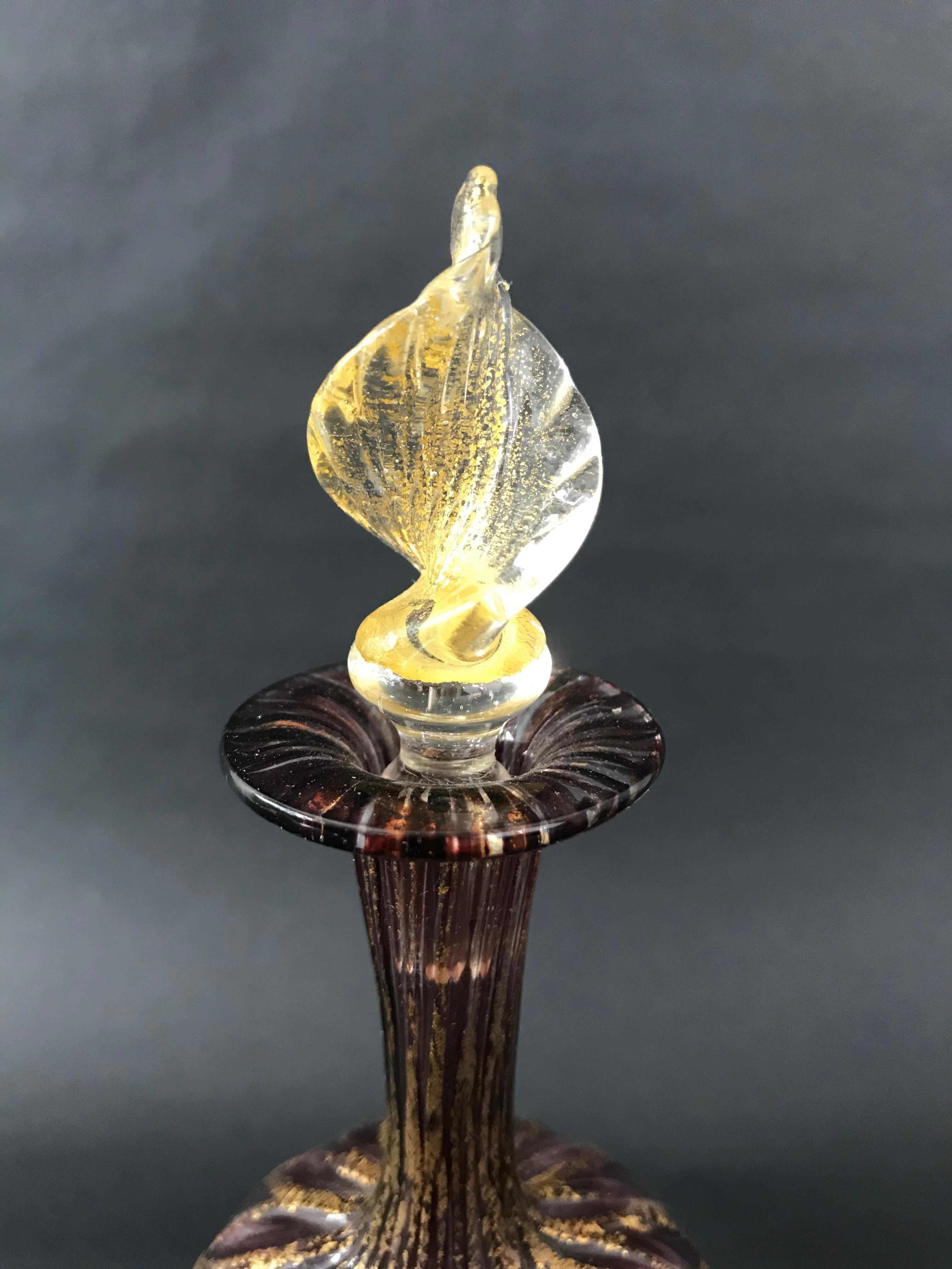 Charming perfume bottle in mauve and gold Murano glass. The neck of the bottle is fluted, the body has a diamond pattern formed by gold inclusions, the stopper forming a spiral leaf also contains gold inclusions.
Italian work of Murano,
end of