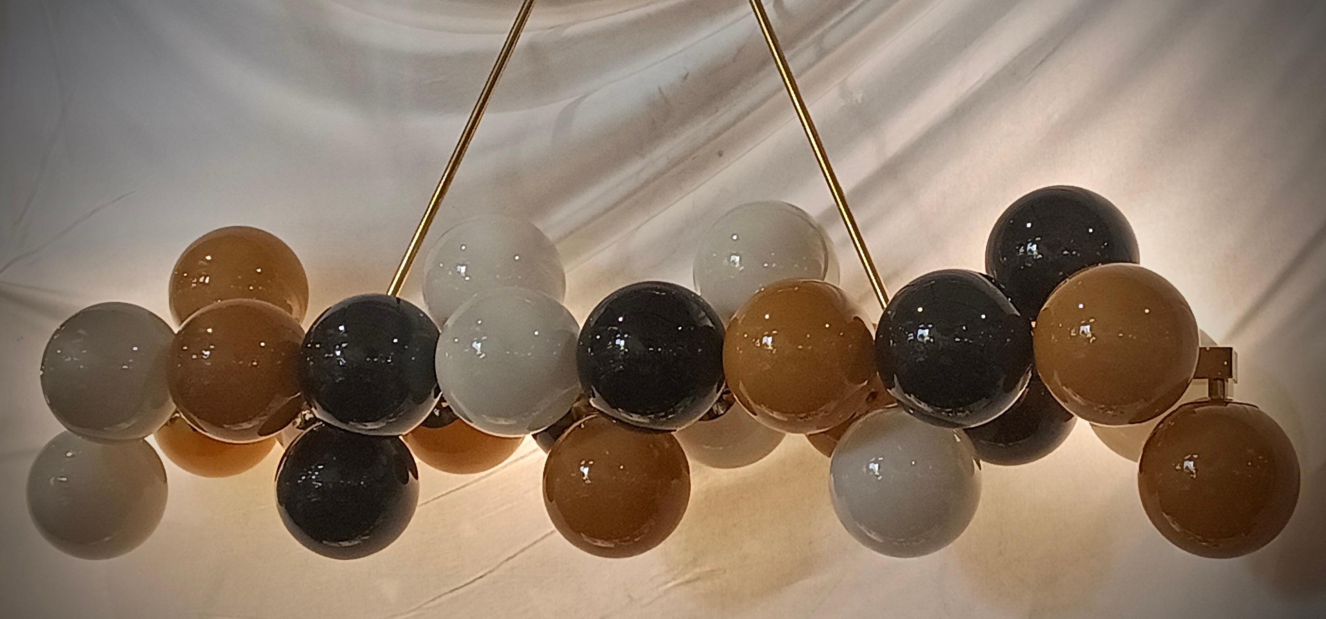 Lampadario di Murano dal design allungato con struttura in ottone e vetri unici dalle molteplici sfumature, nero, bianco e oro. Caratterizzato da semplicità e linearità, il lampadario di Murano presenta una combinazione di splendidi colori con