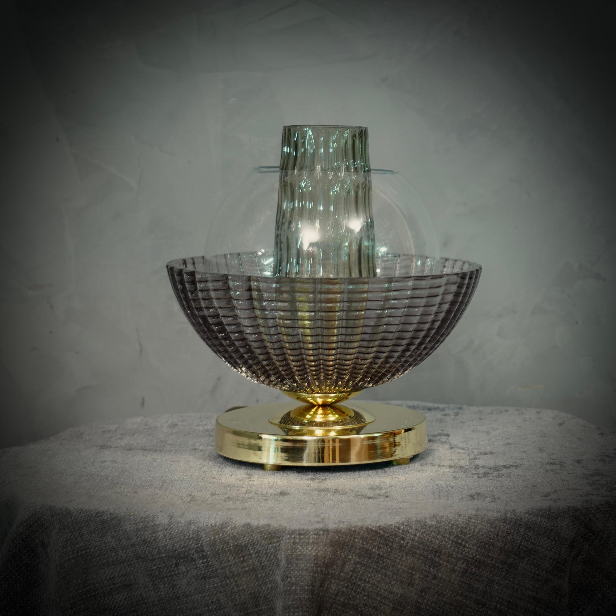 Une lampe de table très spéciale et originale de Murano, une série de verres ronds disposés les uns sur les autres, dans une couleur fumée et laiton. Leur forme est fascinante.

La lampe est composée d'une base ronde en laiton, sur laquelle ont été