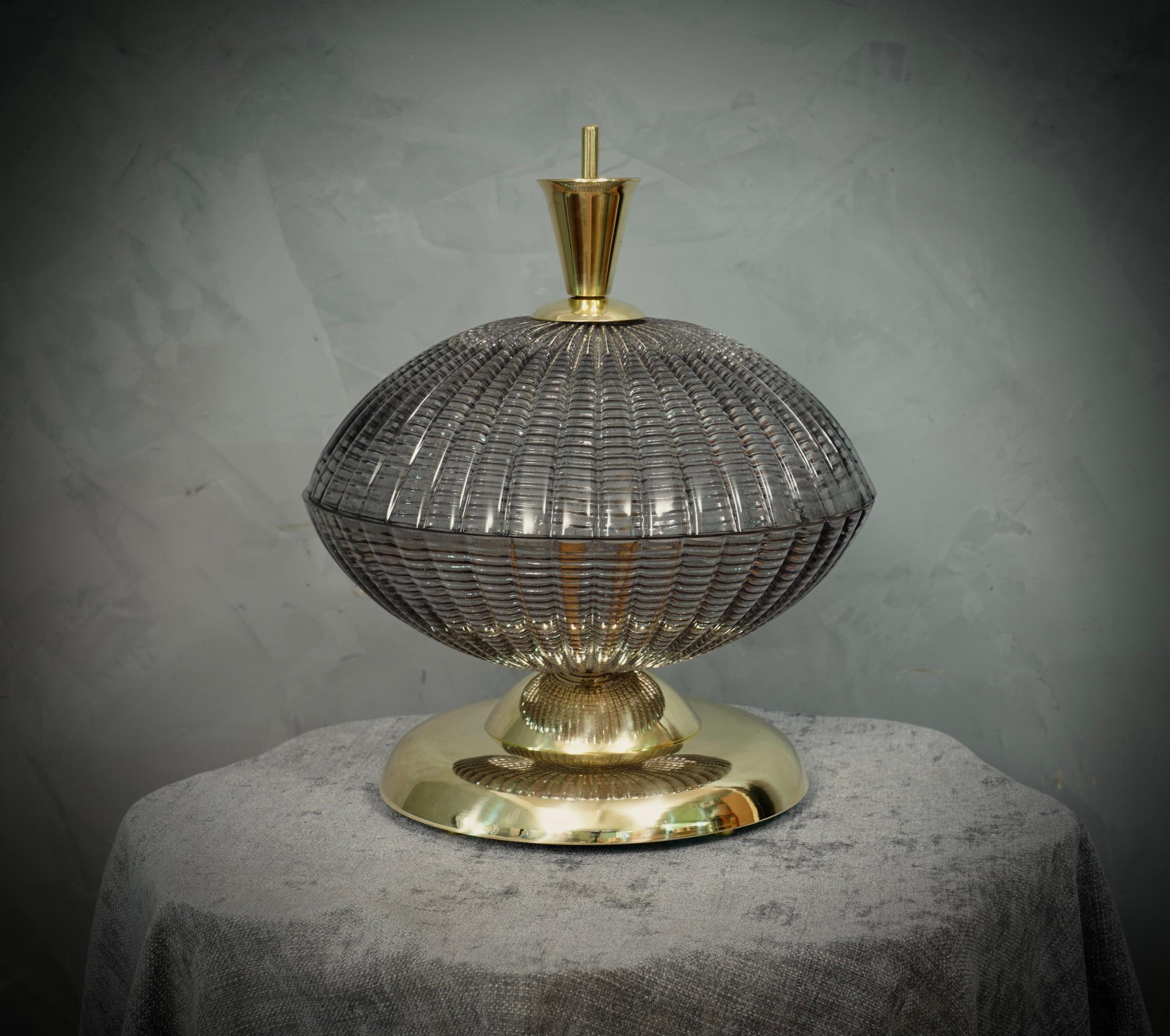 Une lampe de table très spéciale et originale de Murano, une série de verres ronds disposés les uns sur les autres, dans une couleur fumée et laiton. Leur forme est fascinante.

La lampe est composée d'une base ronde en laiton, sur laquelle ont été