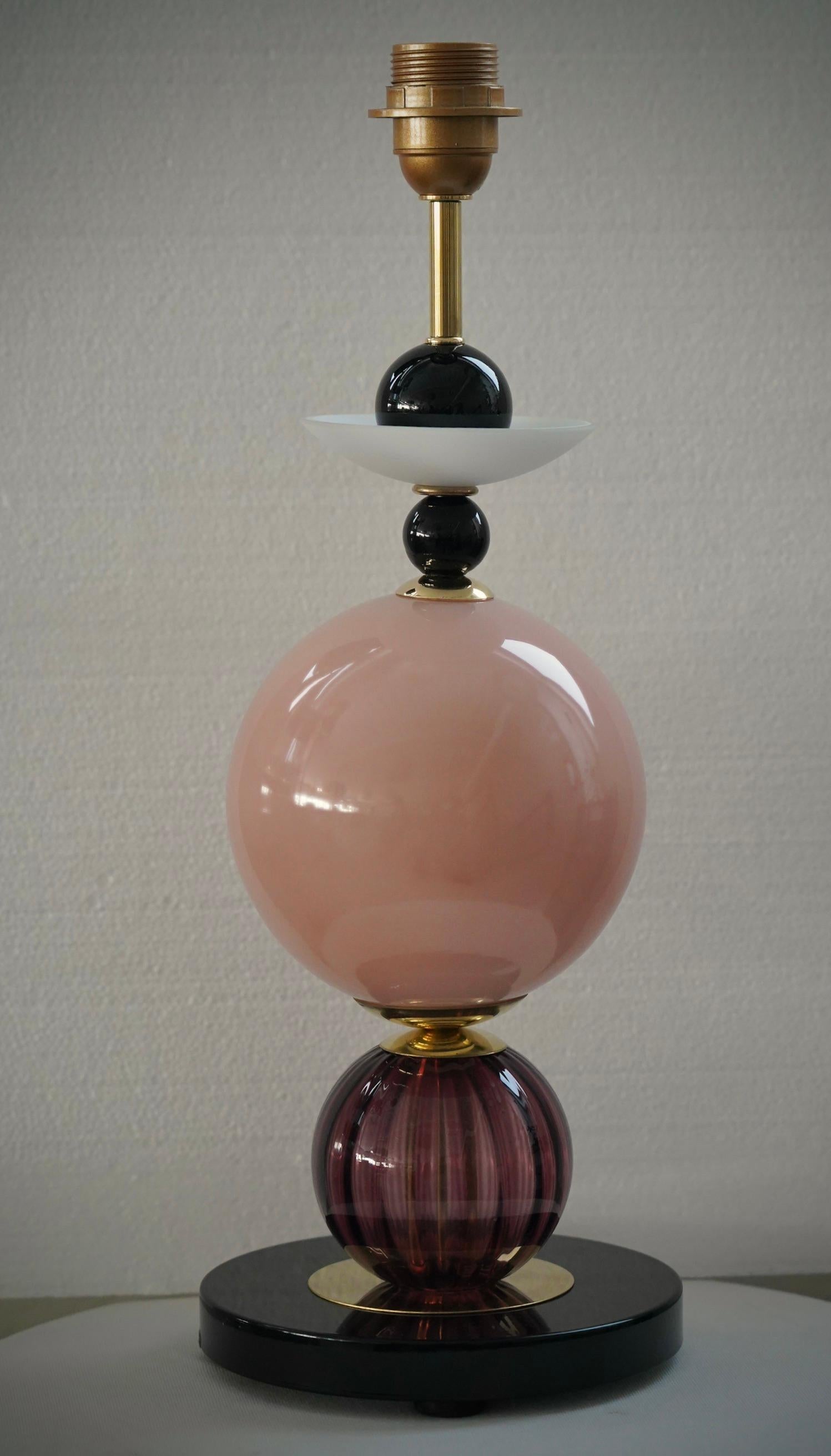 A unique and original Murano glass table lamp sculpture. Its captivating shape is thanks to the unique Murano glass elements.

The lamp is composed of a round black glass base and a stem with pink, purple, and white glass sections inserted into it.