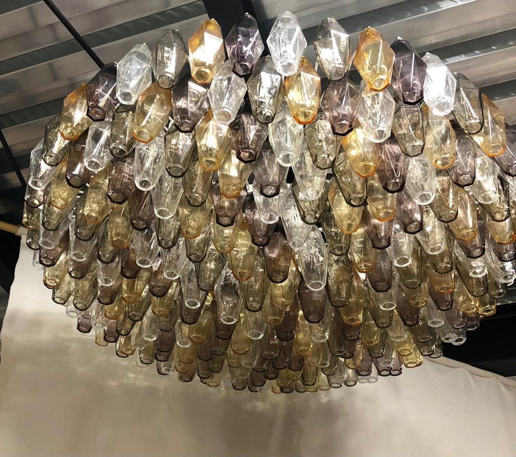 Prächtiger Kronleuchter aus Murano-Glas mit einer besonderen Polychromie, die von transparent über bernsteinfarben bis hin zu bronzefarben reicht. Sein Design ist ebenfalls sehr speziell rund, aber in der Höhe abgeflacht. Die Öfen von Murano