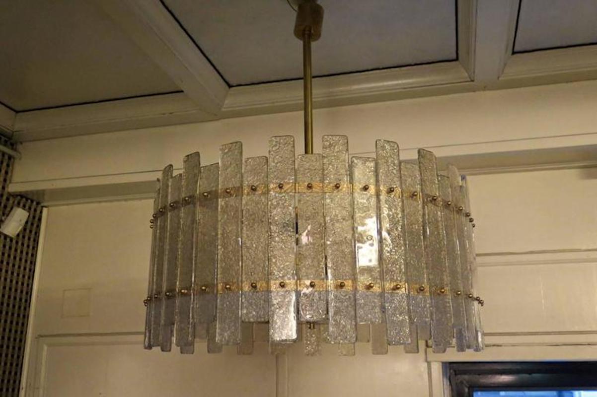 Uno splendido lampadario/soffitto di un sorprendente colore ghiaccio trasparente; un cerchio perfetto di lastre di vetro color ghiaccio.

La sua struttura rotonda è realizzata in ferro color oro, con lastre appositamente tagliate posizionate lungo