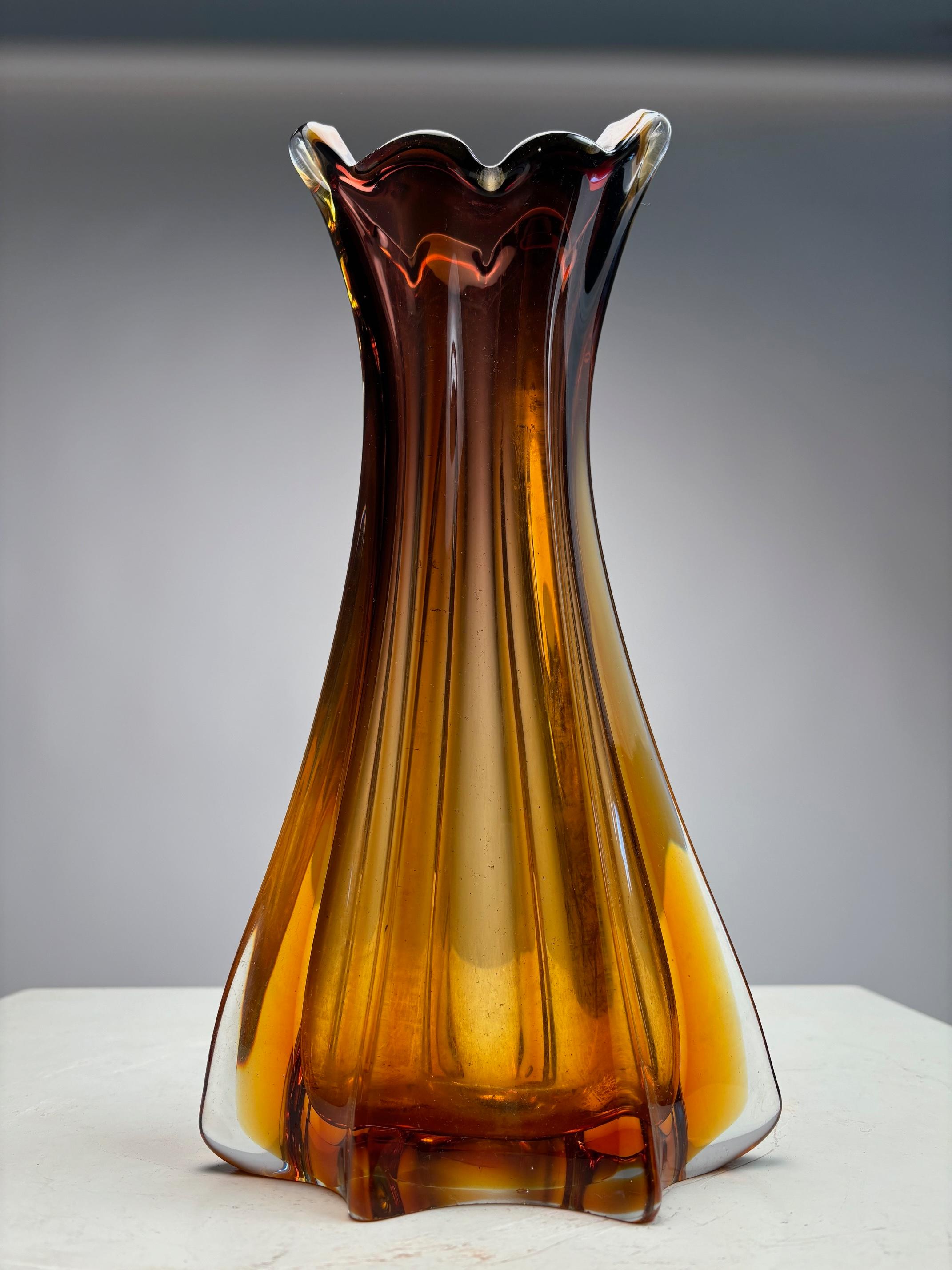 This vase, made around 1960 in a Murano furnace, belongs to the heavy, double-layered submerged family: a core of amber glass (from deep brown to pale honey) completely enveloped by a layer of colorless crystal of extraordinary thickness, up to 18
