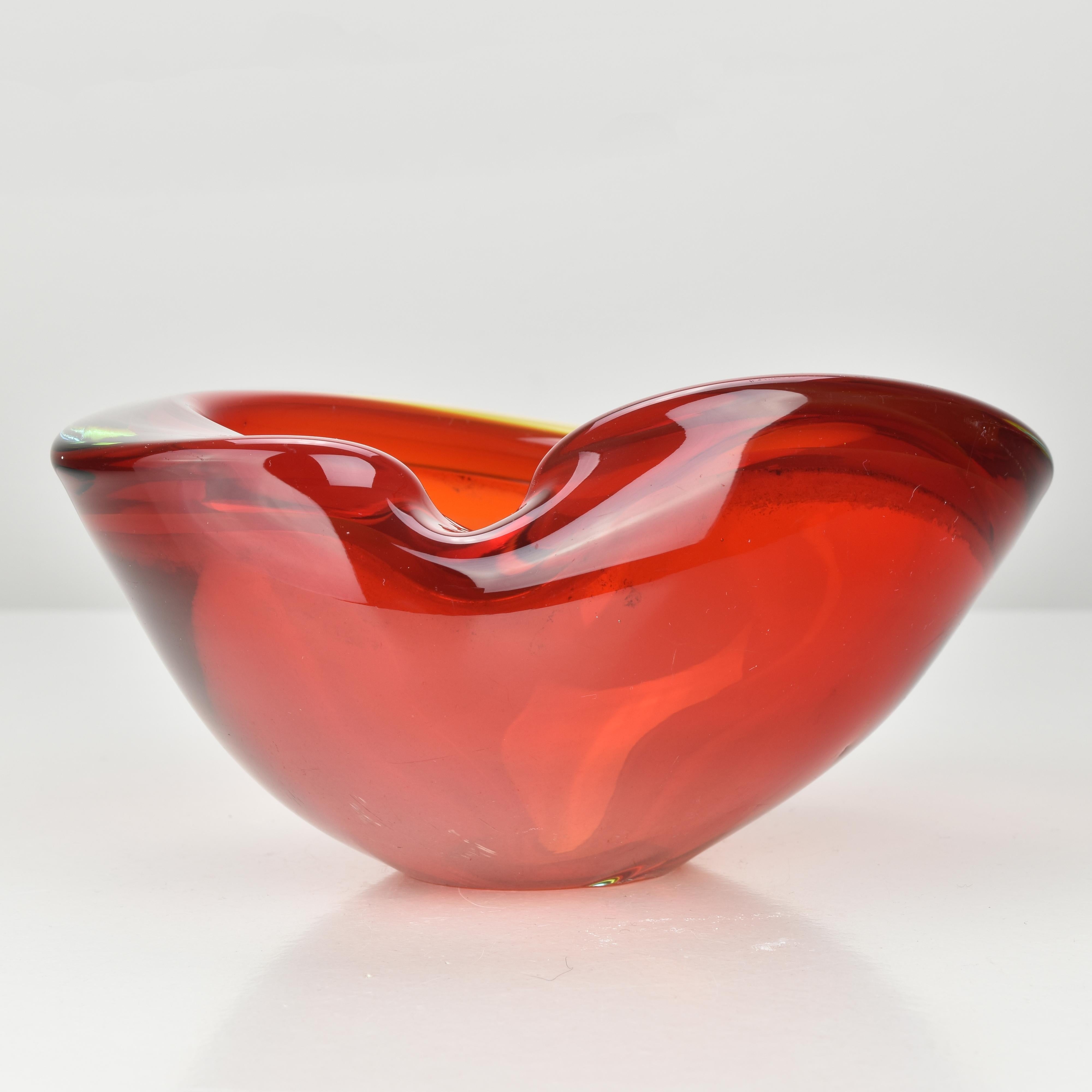 Un vibrante cuenco de cristal artístico de Murano Sommerso atribuido a Flavio Poli, con un llamativo núcleo interior rojo que pasa sutilmente a cálidos tonos ámbar y humo suave. Esta pieza muestra una expresiva forma orgánica con un borde fluido y
