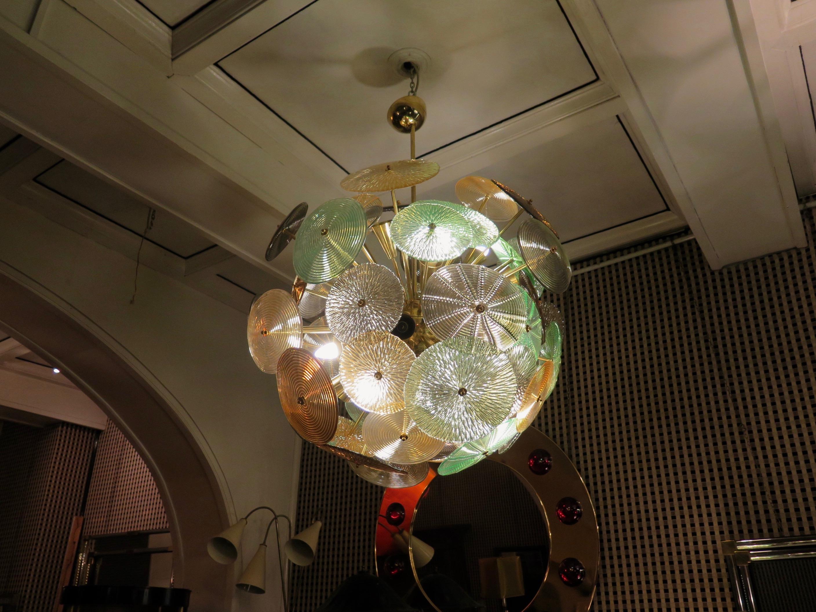 The large glass multicolored disks make up this Murano chandelier from the 1960. A Classic Sputnik from the middle of the century.

Made of a large central sphere in which brass rods are screwed, glass disks are placed above the brass rods. Of