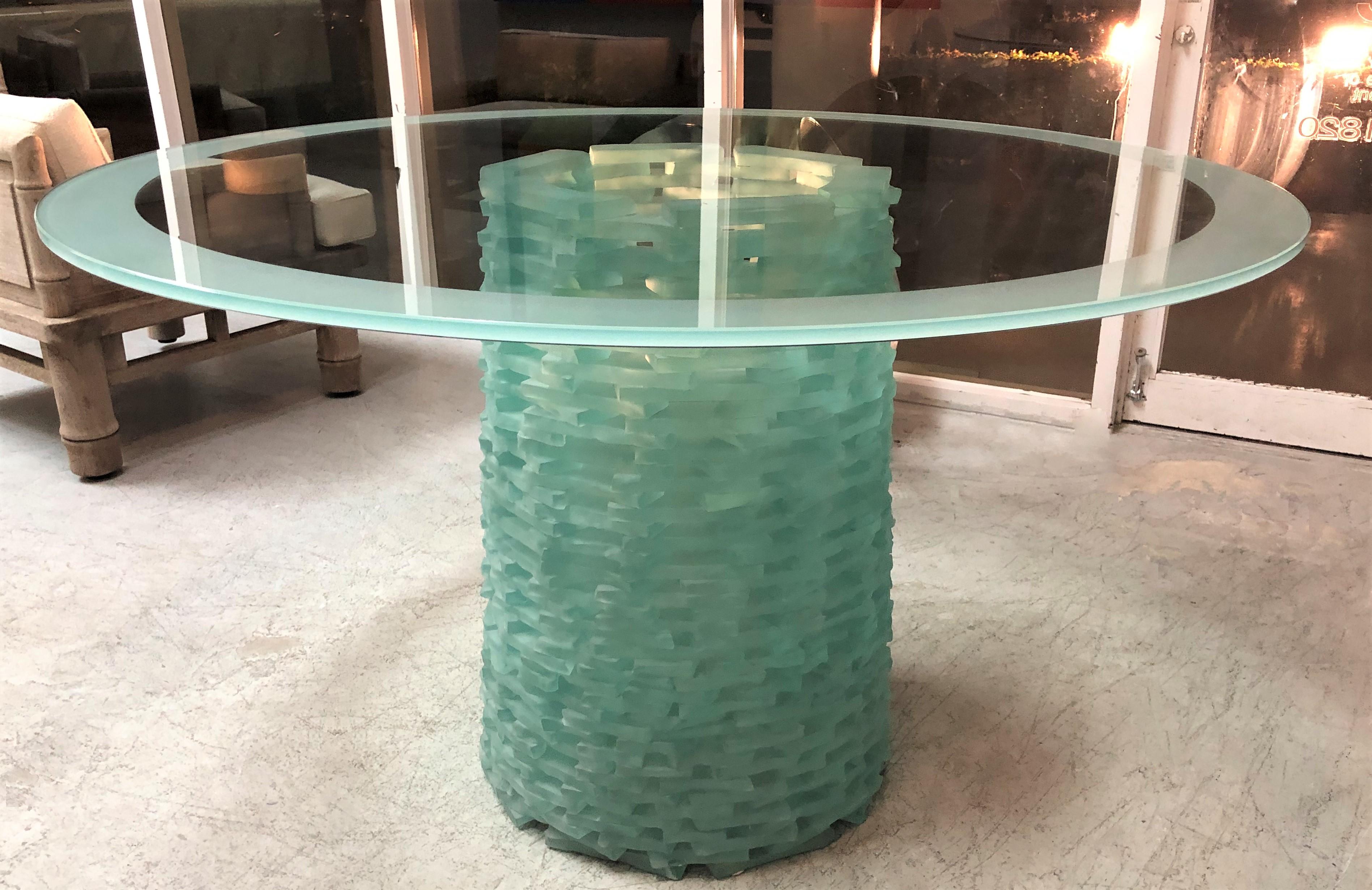 A round sculptural glass table. The base is made with stacked free form pieces of glass that have been sandblasted. The top is clear glass with and etched edge. The base has a restrained luminous quality and it is 18