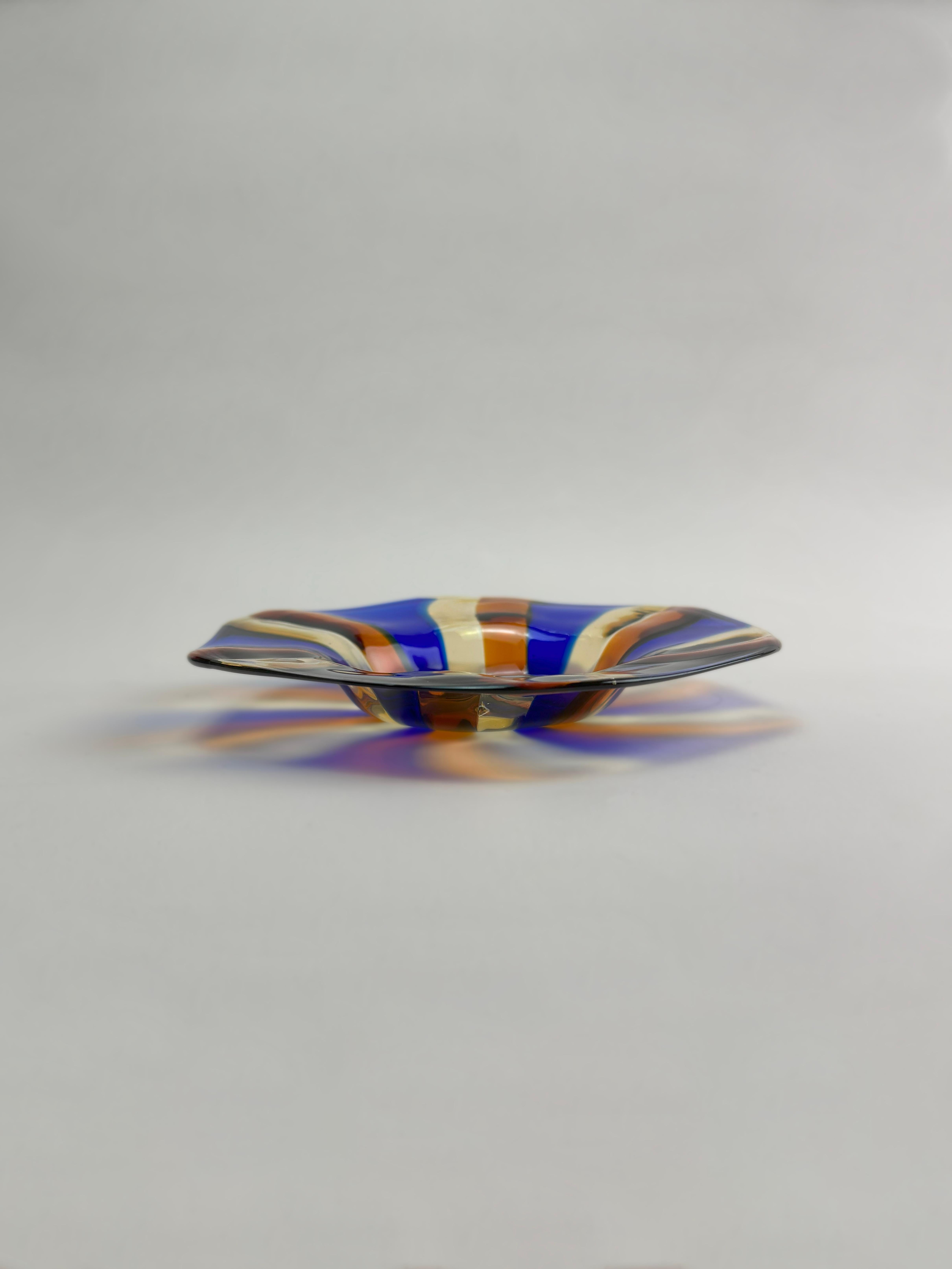 A vibrant Murano glass candy dish, attributed to the furnace of Fratelli Toso and dating to the 1970s. Crafted in a softly hexagonal form, the dish features alternating bands of cobalt blue, amber red, and clear glass, radiating outward in a dynamic