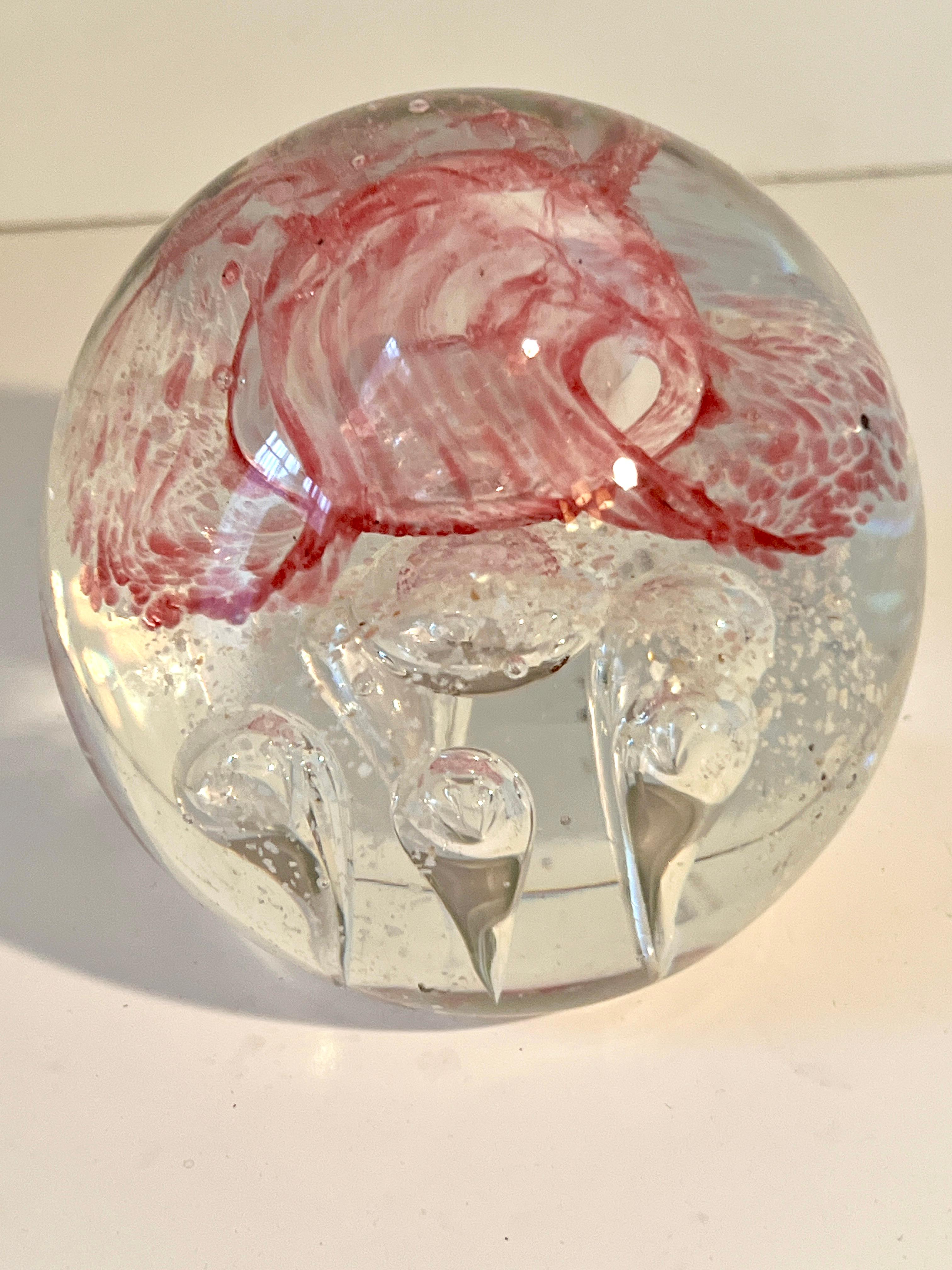 Un magnifique poids de papier en verre avec de grosses bulles, souvent symétriques, et un joli ruban rouge en spirale à l'intérieur.

Un complément à tout bureau, poste de travail ou comme élément décoratif sur une table de cocktail.  La pièce est