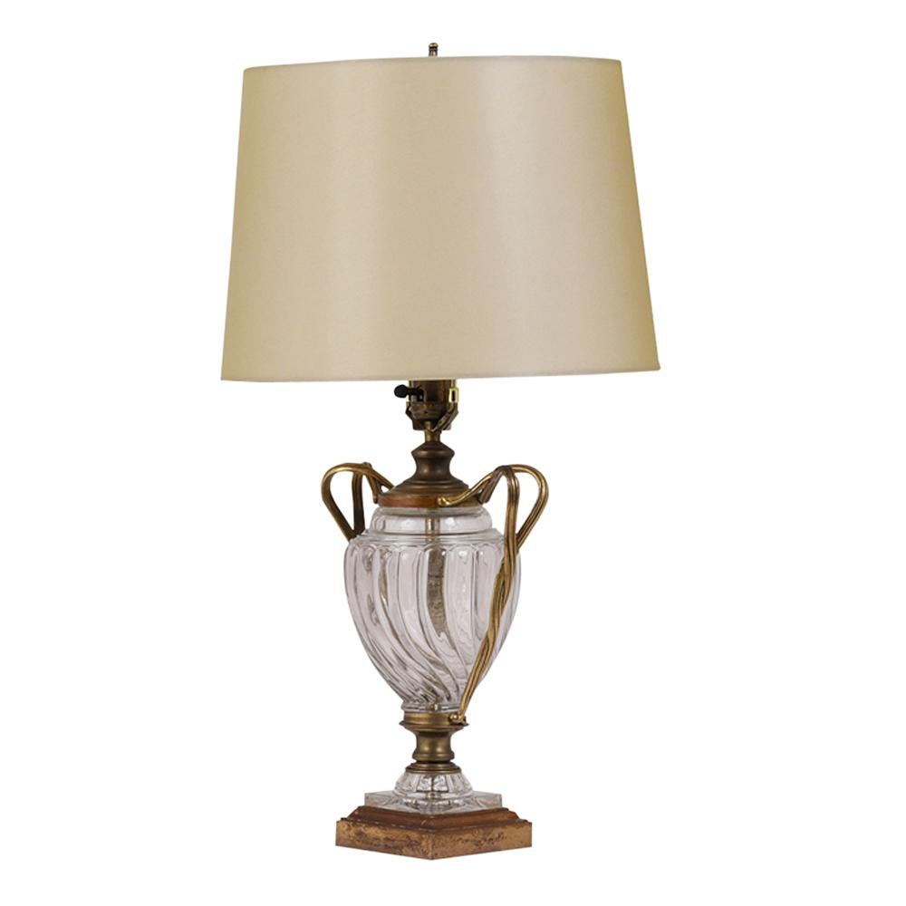 This Murano Regency style glass table lamp is in great condition. The lamp features a glass urn design base with brass handles, new shade and brass top finial. The glass is in great condition and has no chips or cracks. It is wired to US standards