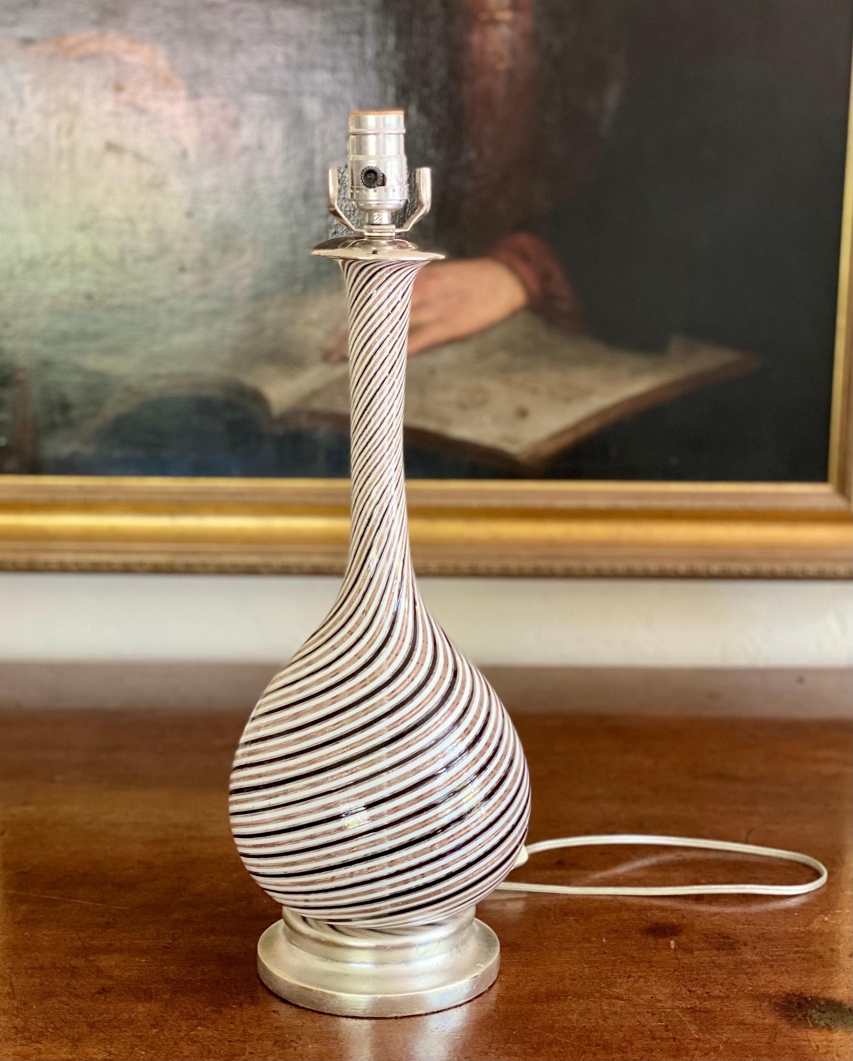 A very fine, beautifully shaped Murano glass lamp, with clear glass and swirls in soft black tones
and alternating gold with gilded flecks. The base has been gilded in white gold. 
Harp, bulb, shade and finial not included.