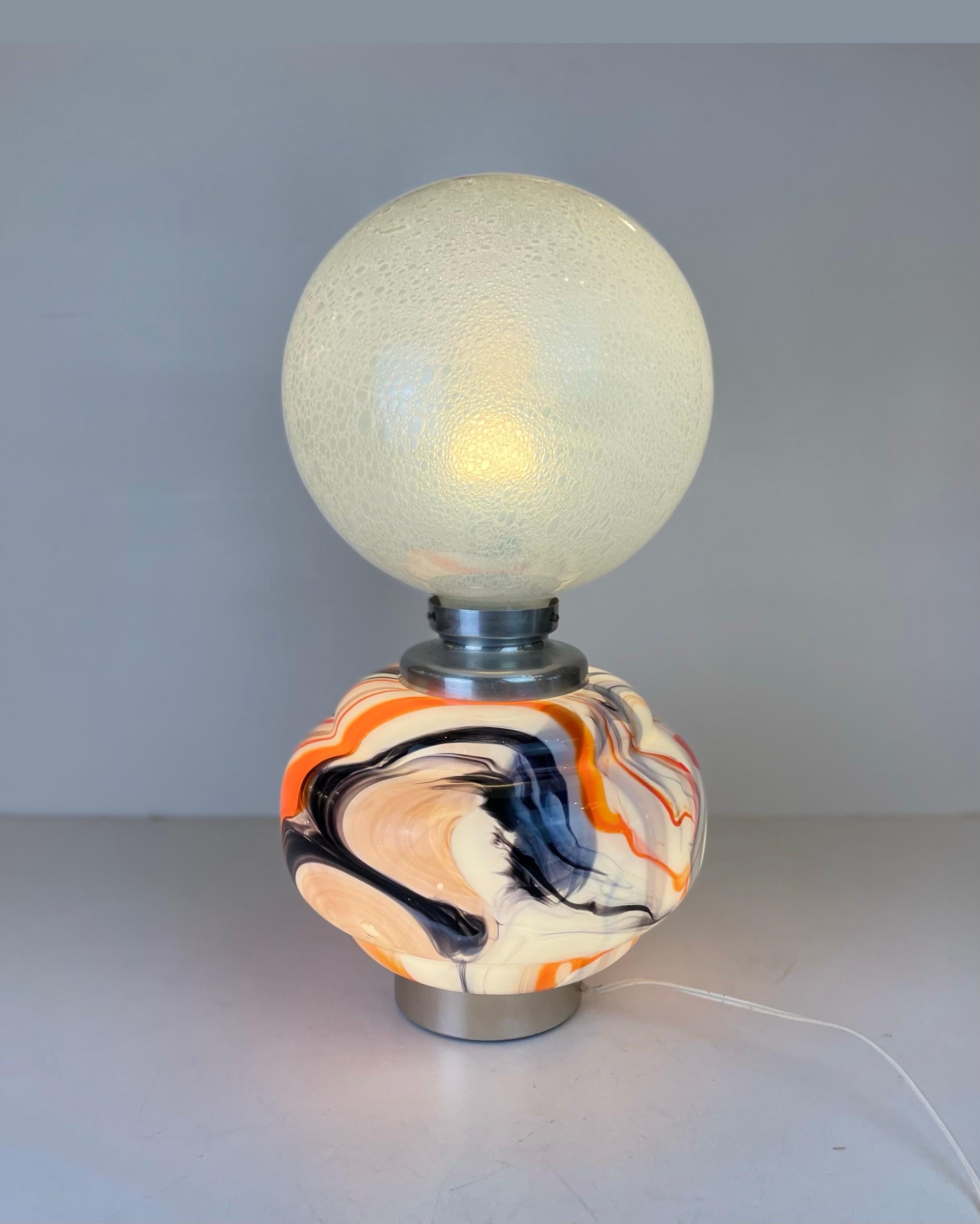 Preciosa lámpara de sobremesa de dos fuentes, fabricada con dos piezas de cristal de Murano sobre un soporte cepillado y cromado. De color en la parte inferior y burbujeante en la superior, ambas pueden encenderse independientemente.
-
Producido en: