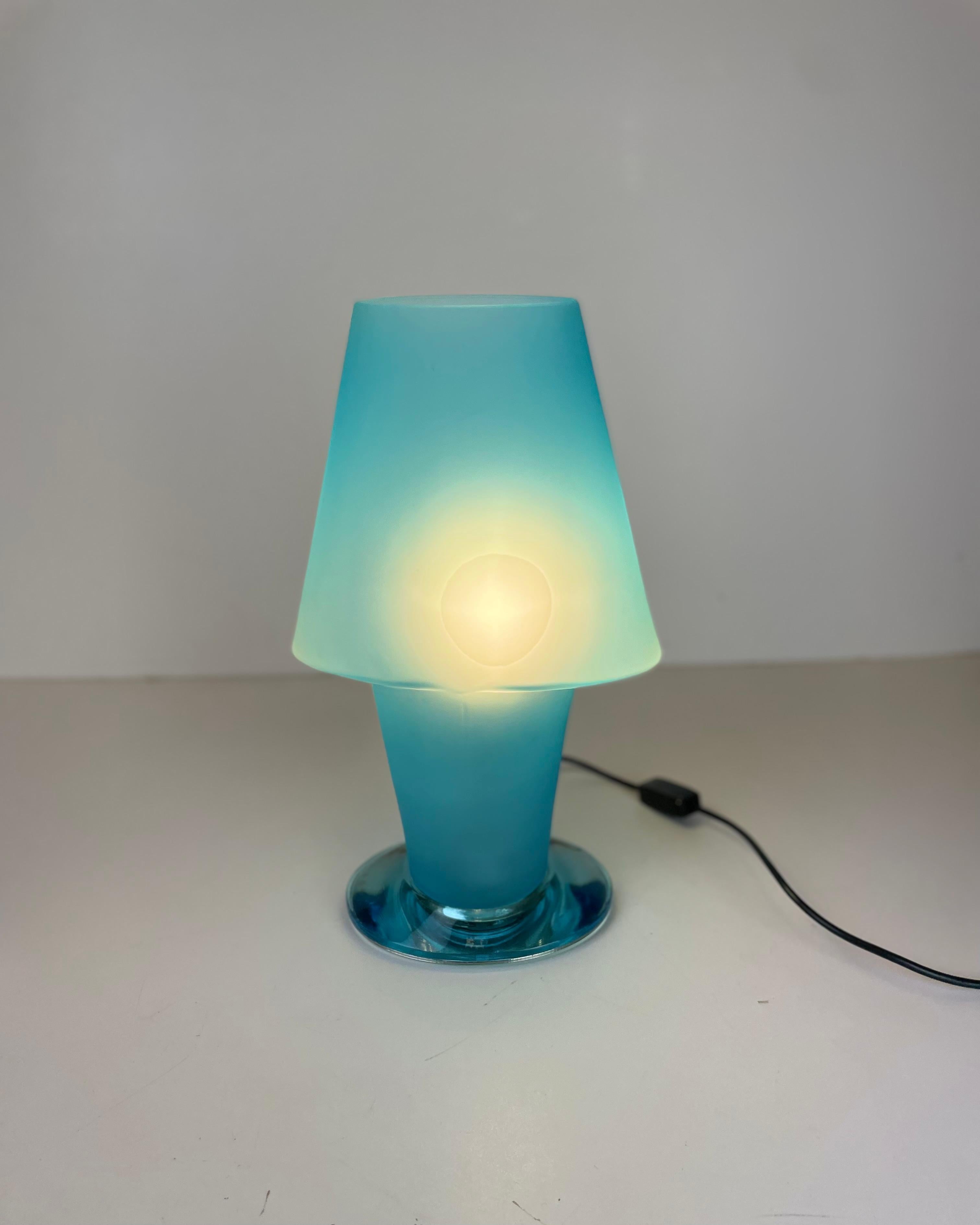 Lampe de table italienne réalisée à partir d'une seule pièce de verre bleu dépoli de Murano, posée sur un bloc de verre bleu transparent de Murano, sous une feuille de métal qui donne de la profondeur à l'ensemble. Conçu dans le style de Daniela
