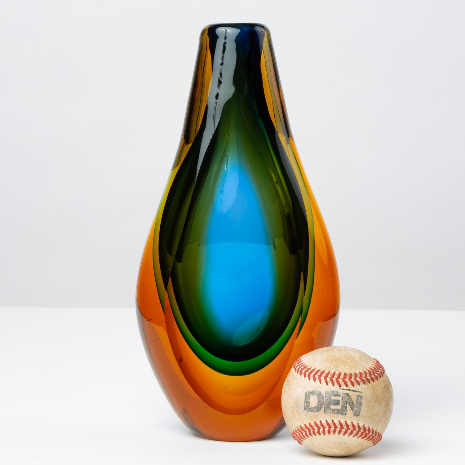 A colorful Murano art glass vase with a tulip shape and narrow profile. The triple Sommerso technique suspends a teardrop formation of blue inside a layer of green, both encased in the amber-colored glass outside. The two ground edges refract the