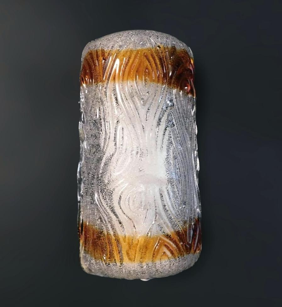 Italian wall light with a clear and amber trunk shaped Murano glass shade hand blown in Graniglia technique to produce granular textured effect, mounted on white metal frame / Made in Italy by Mazzega circa 1960s
Measures: Height 12 inches, width 6