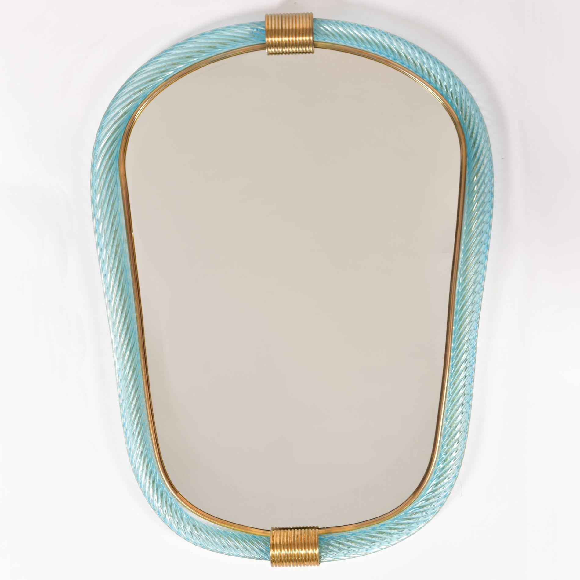 Paire de miroirs eliptiques en verre de Murano soufflé à la main, à côtes vert pâle/bleu, avec deux fermoirs cannelés en laiton en haut et en bas, le bord intérieur étant bordé d'un mince filet en laiton.

Existe aussi en rose pâle.

Délai de 8 à 9