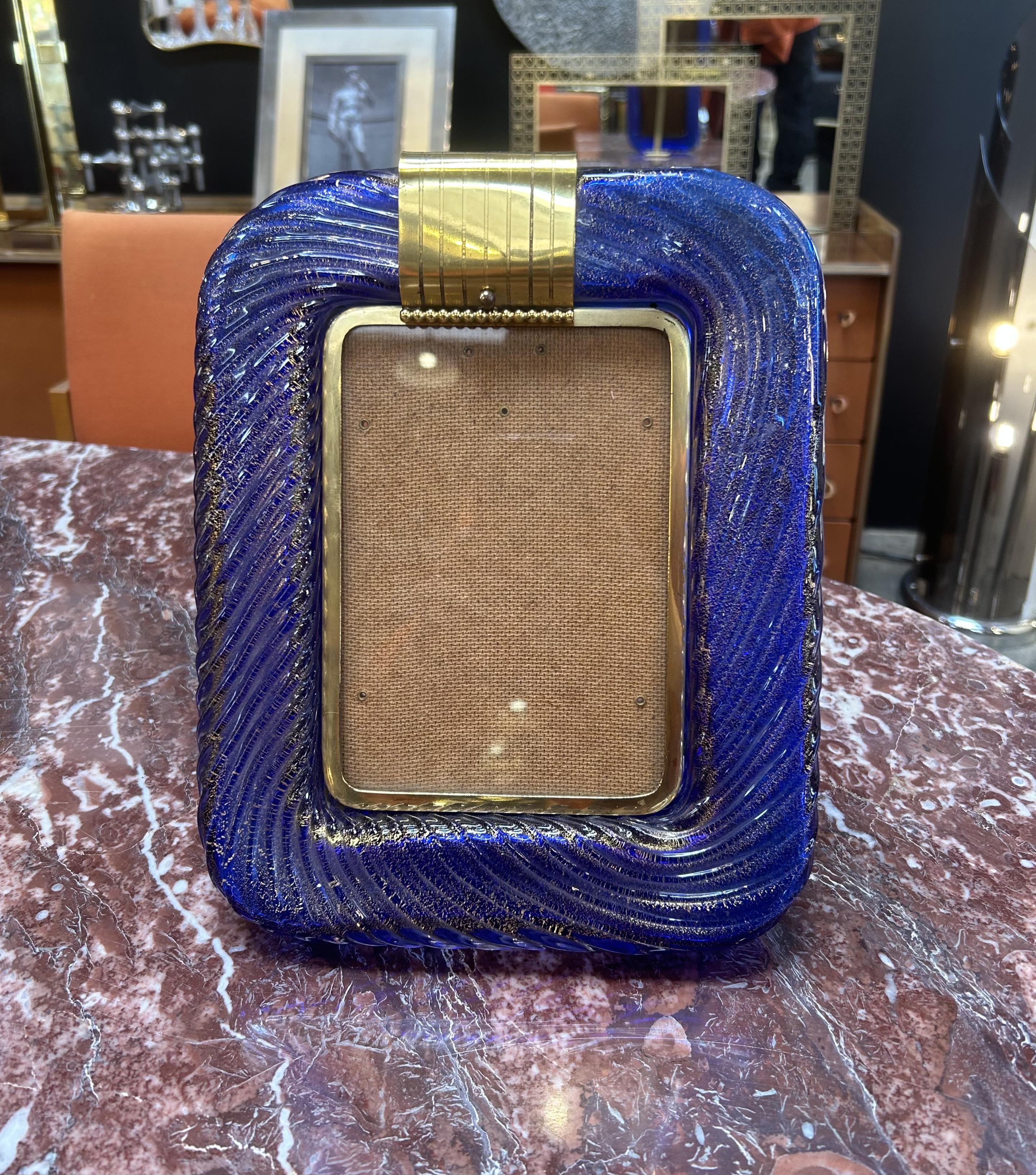 This vibrant cobalt blue Murano glass Italian picture frame, crafted in the 1950s or 1960s, is delicately swirled with gold flecks, creating a rich, textured appearance that catches the light beautifully. Framed by elegant brass details, including a