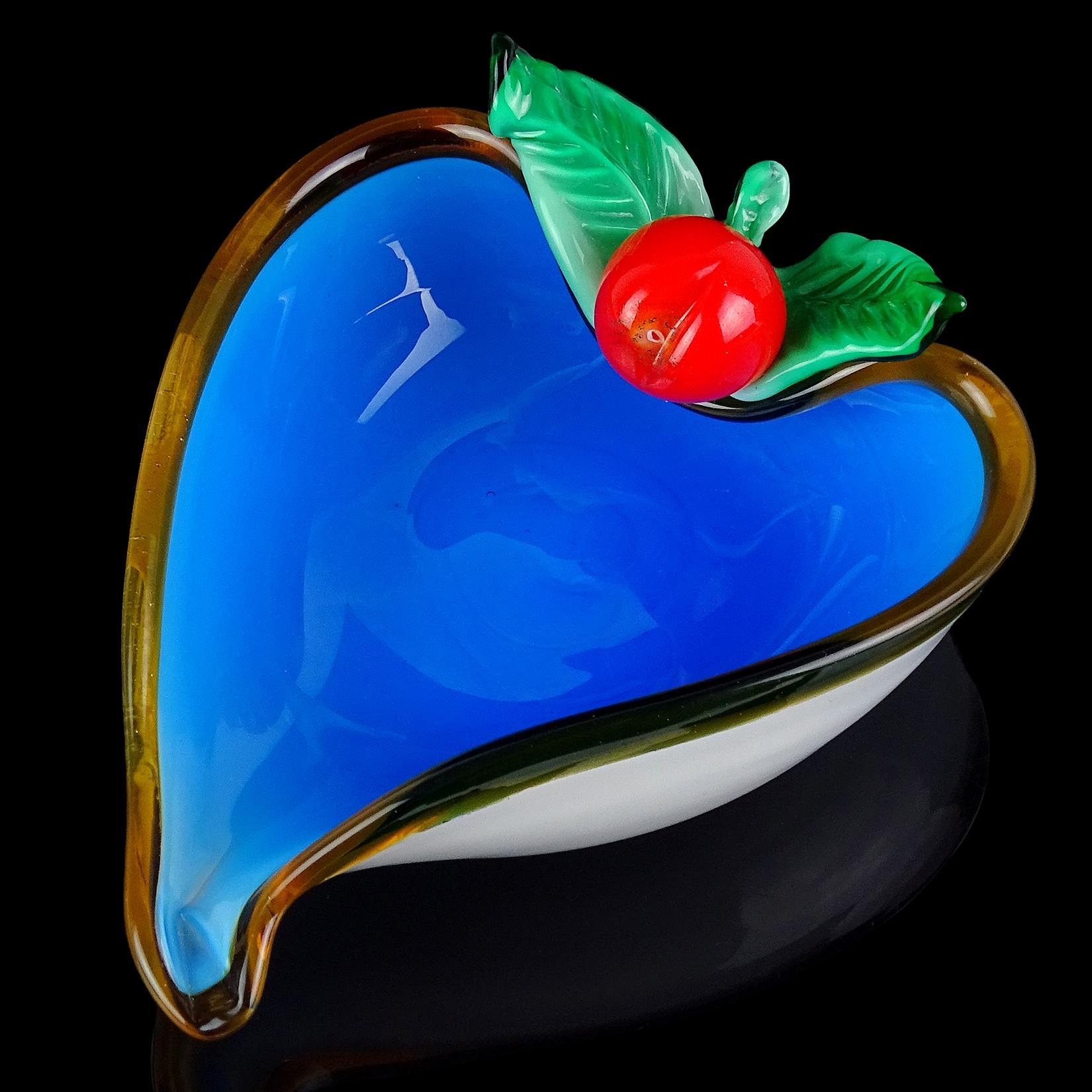 Beautiful vintage Murano hand blown white over cobalt blue Italian art glass trinket dish, vide-poche. The piece has an applied red cherry with green leaves decoration, and amber lined rim. The bowl also has a heart shape. It still retains an old