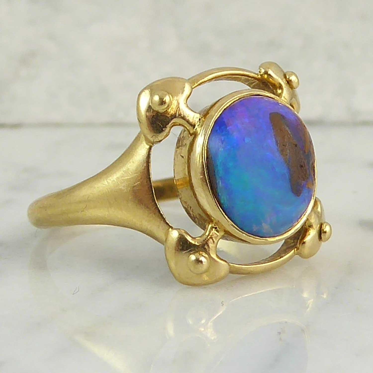 A Murrle Bennett & Co opal ring in a typical Arts and Crafts design and using a boulder opal in all its natural and unadorned beauty.  The opal shows lilac, blue and green colours arouond the boulder which sits off centre to one edge of the