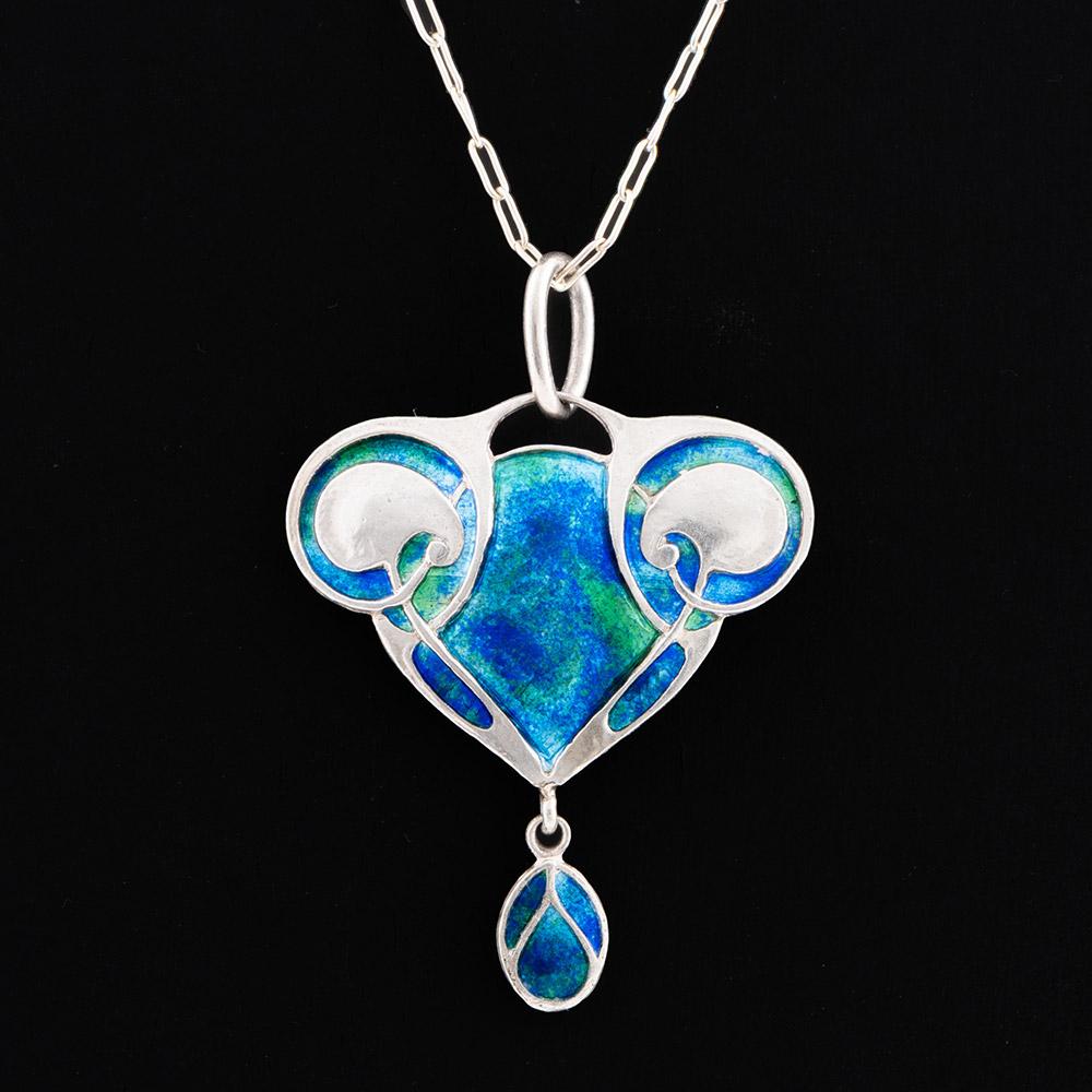Encabezamiento : Collar colgante Murrle Bennett de plata y esmalte
Fecha : c1910
Origen : Marca impresa en revés MBCo y 950. Probablemente fabricado en Pforzheim, Alemania
Decoración : Vivo esmalte azul y verde a cada lado de un par de hojas