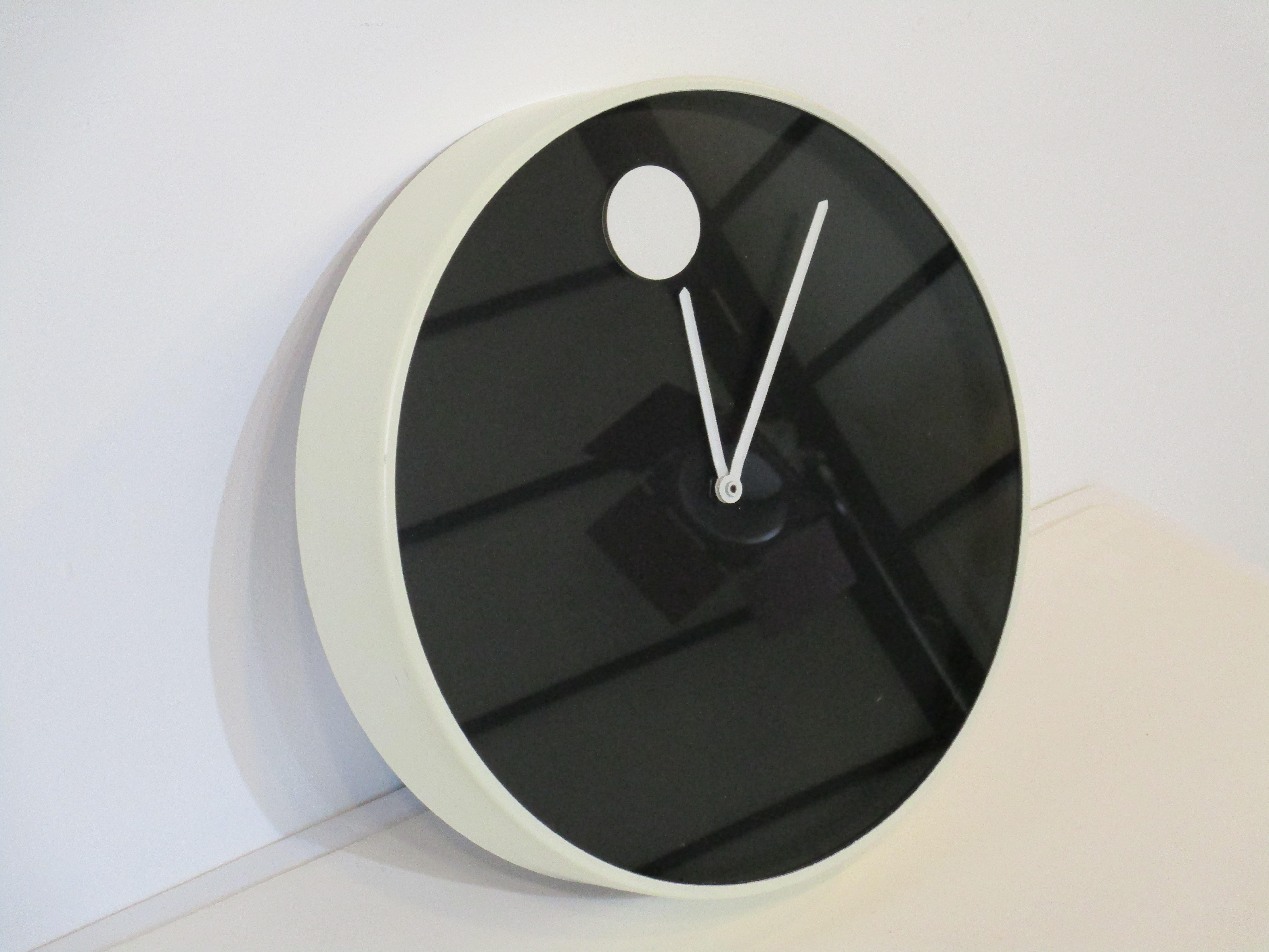 A white metal framed clock with satin black face having a large white dot at twelve o'clock with hour and minute hand. An iconic 1970's design that is included in the collection of the Modern Museum of Art so the name 