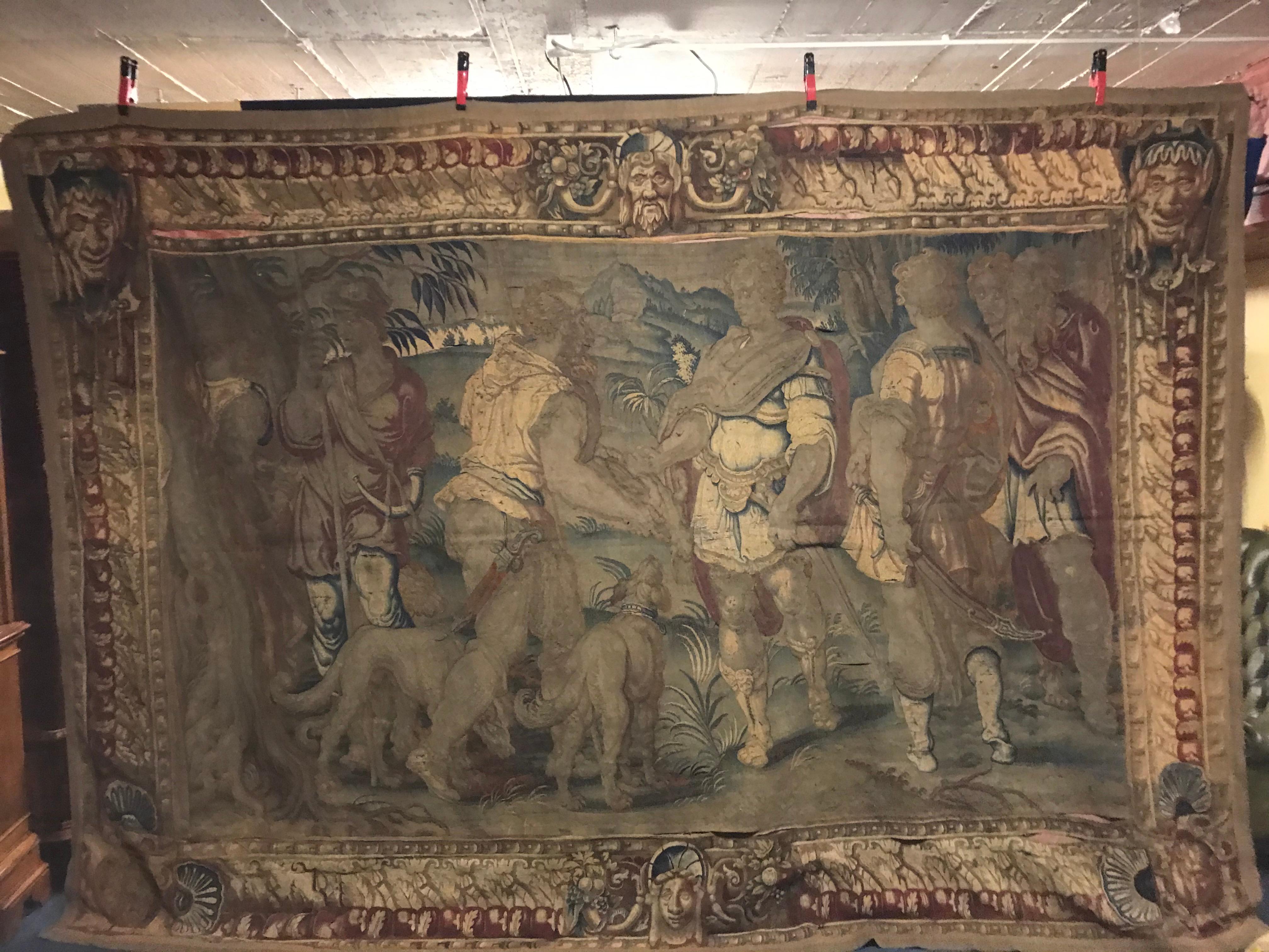 Large tapestry canvas.
Probably Flemish 16th-17th century hunting scene in the Renaissance style,
male hunting party and hunting dogs in a wide landscape with mountains in the background,
wide border with acanthus and scrollwork cartouches with