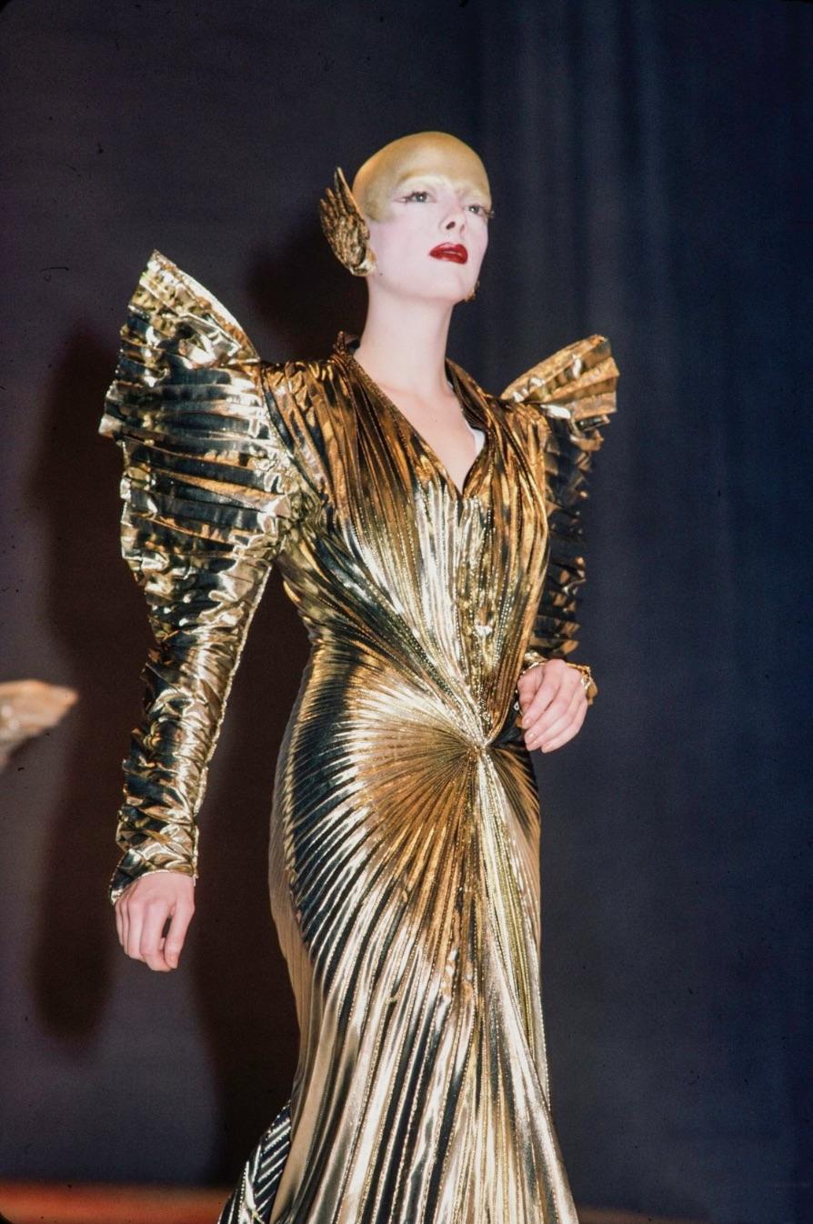 This is an exceptionally rare and iconic gown from Thierry Mugler’s Fall 1984 runway collection, L’Hiver des Anges. Crafted in radiant gold silk lamé, the design is inspired by celestial beings—angels, saints, and the Virgin—capturing the divine