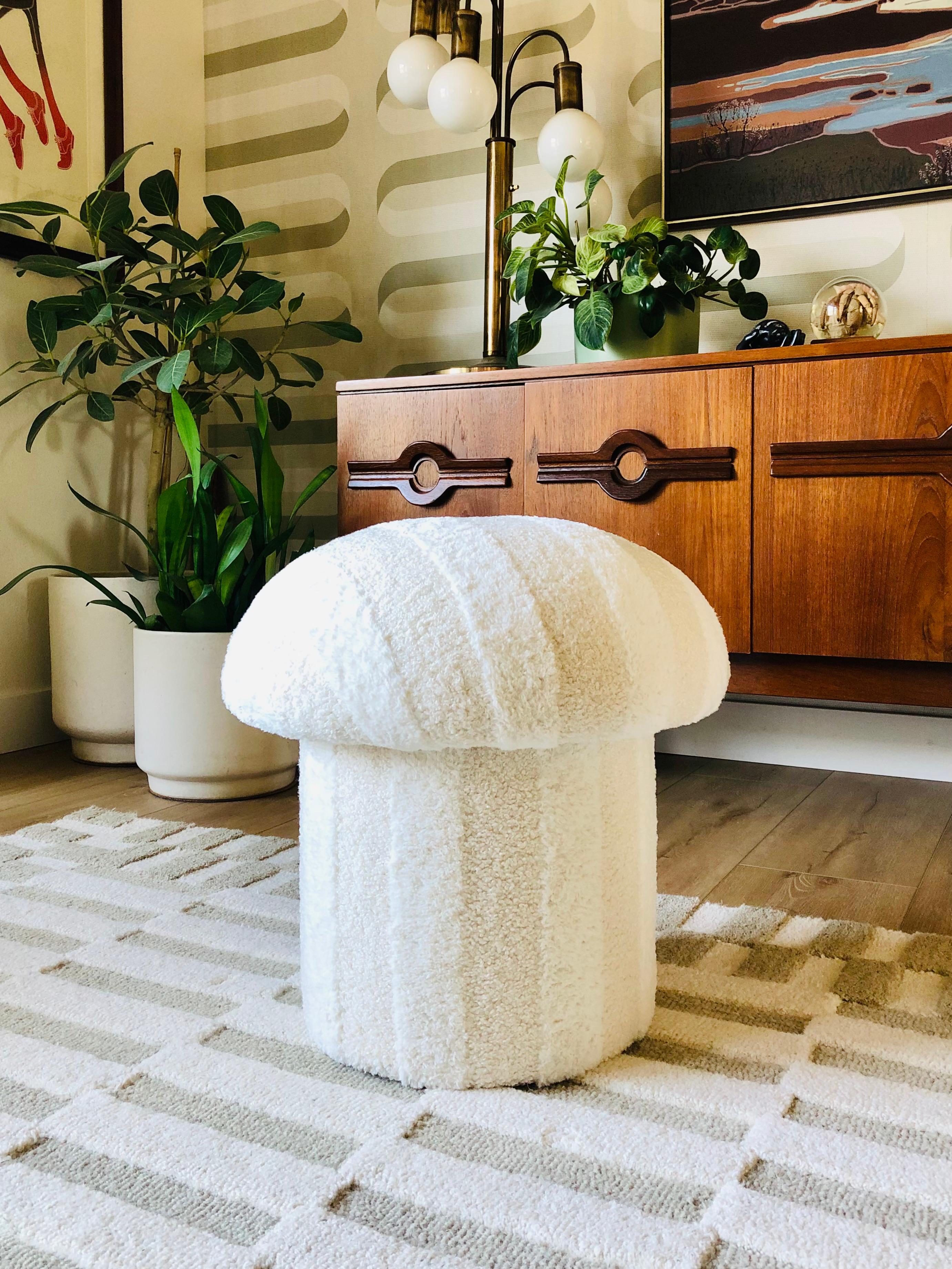 A handmade mushroom shaped ottoman, upholstered in a striped plush fabric. This plush fabric consists of alternating neutral bands of white plush and curly ivory boucle. Perfect for using as a footstool or extra occasional seating. A comfortable