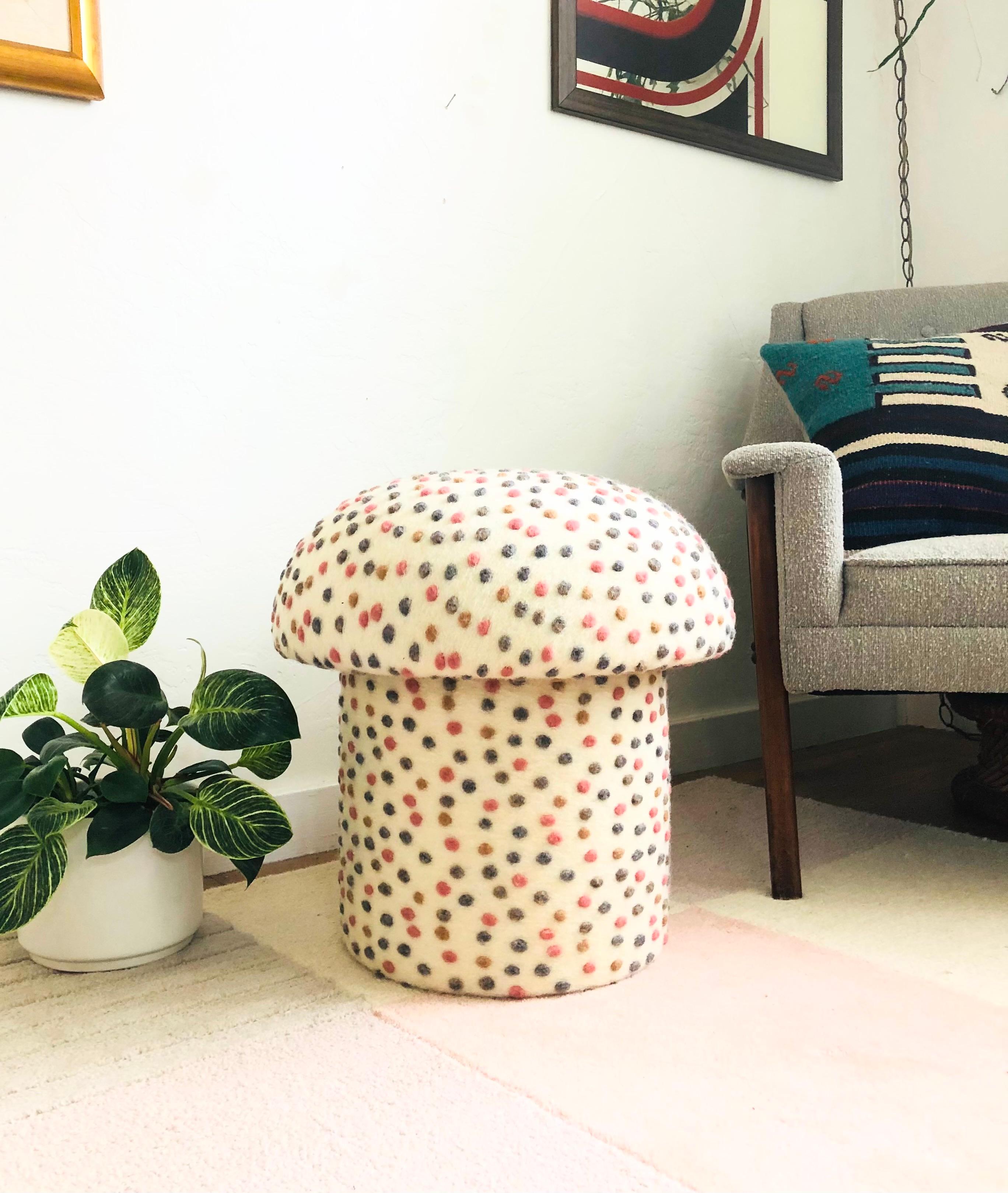 A handmade mushroom shaped ottoman, upholstered in a dotted wool blend fabric. Perfect for using as a footstool or extra occasional seating. A comfortable cushioned seat and sculptural accent piece. Fabric is a cream color with small textured dots