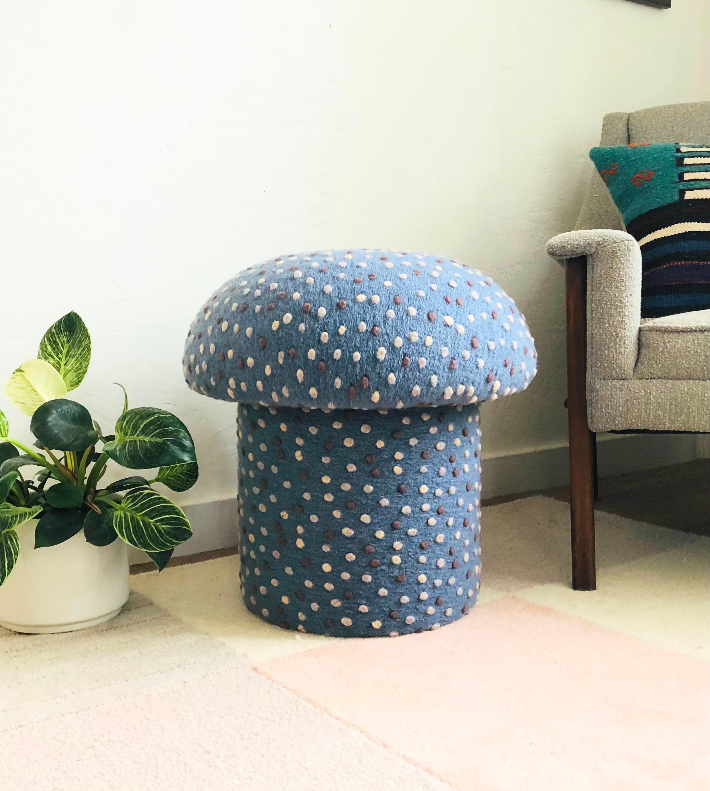 A handmade mushroom shaped ottoman, upholstered in a dotted wool blend fabric. Perfect for using as a footstool or extra occasional seating. A comfortable cushioned seat and sculptural accent piece. Fabric is a light denim blue color with small