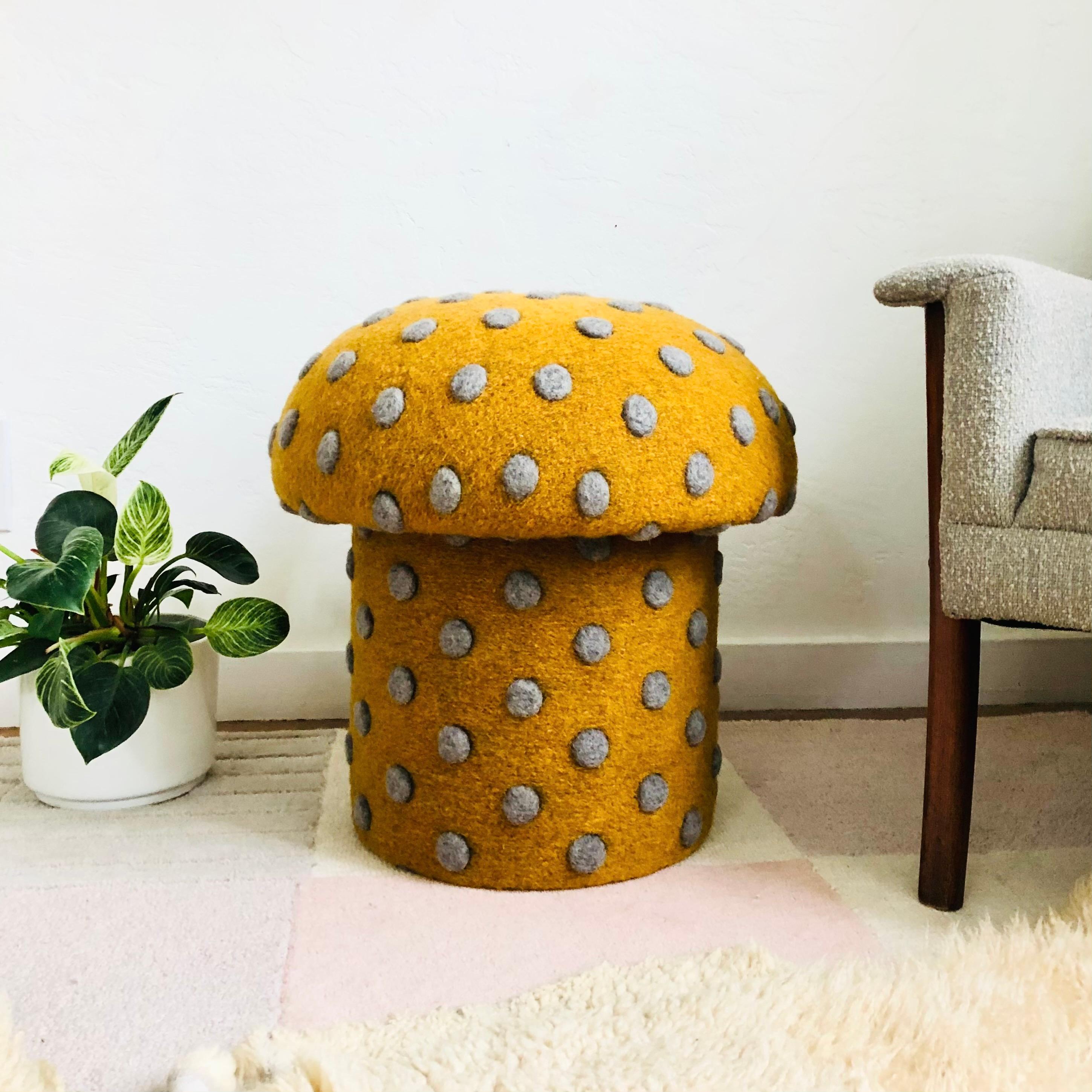 A handmade mushroom shaped ottoman, upholstered in a dotted wool blend fabric. Perfect for using as a footstool or extra occasional seating. A comfortable cushioned seat and sculptural accent piece. Fabric is an ochre color with large textured gray