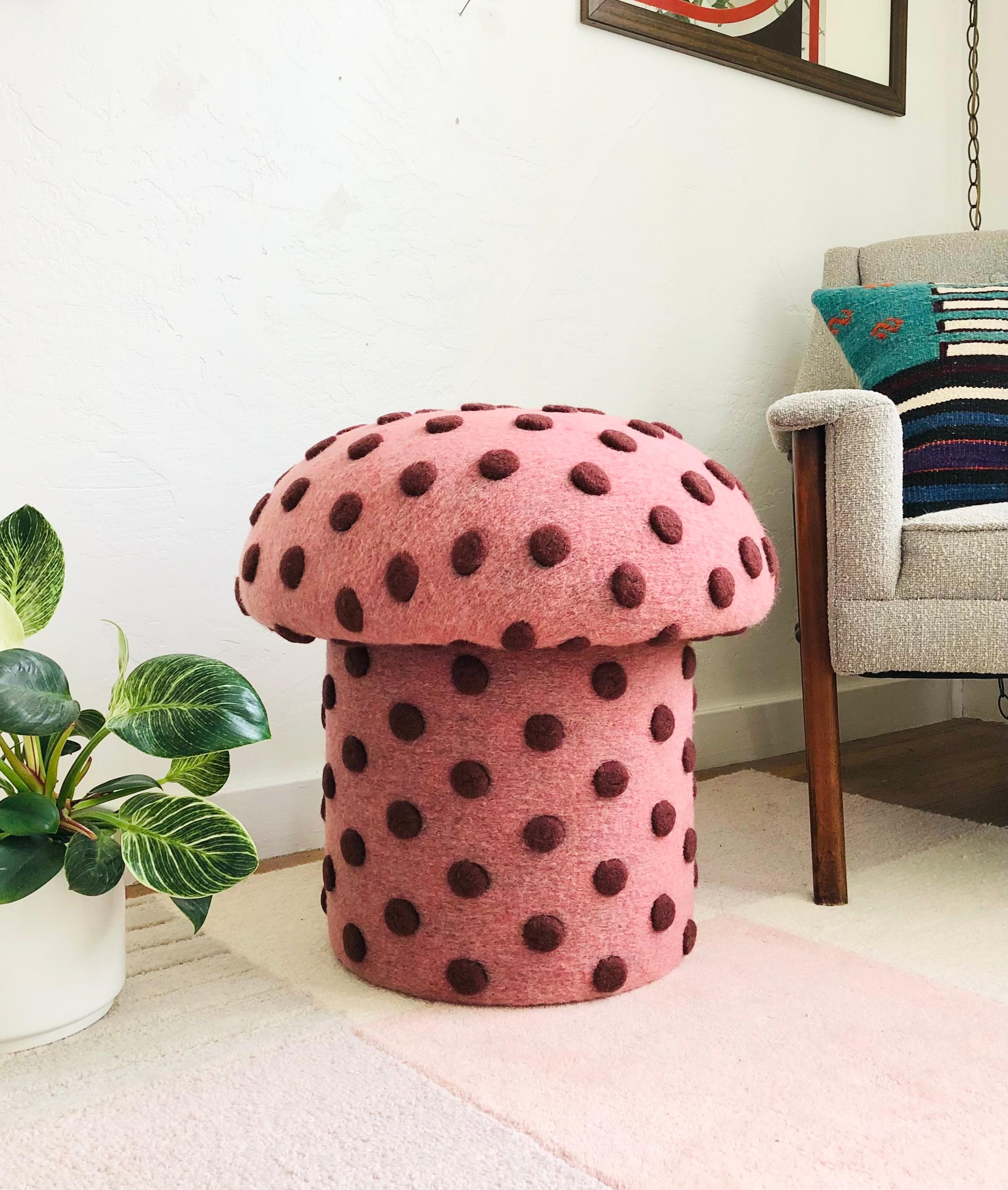 A handmade mushroom shaped ottoman, upholstered in a dotted wool blend fabric. Perfect for using as a footstool or extra occasional seating. A comfortable cushioned seat and sculptural accent piece. Fabric is a pink color with large textured