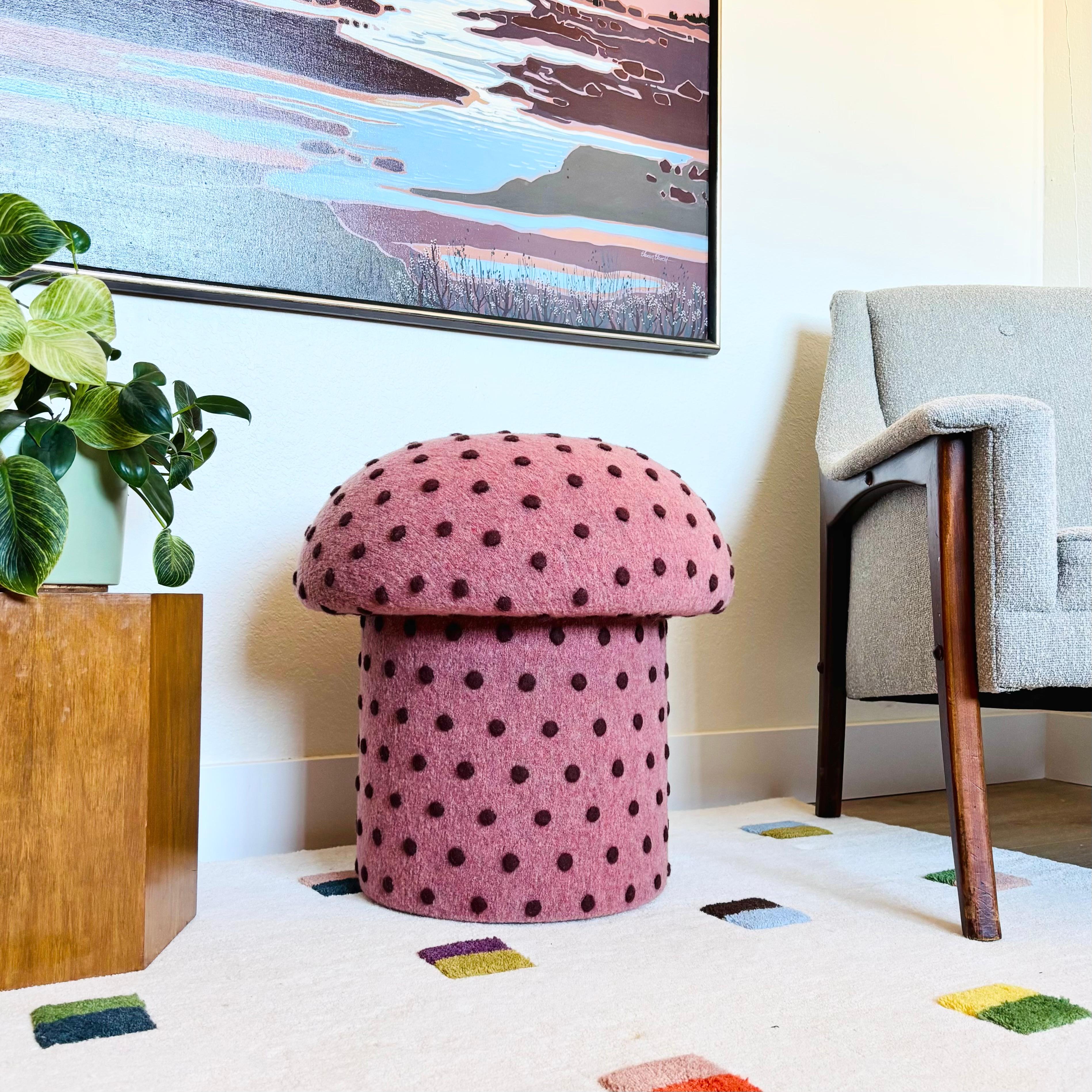 A handmade mushroom shaped ottoman, upholstered in a dotted wool blend fabric. Perfect for using as a footstool or extra occasional seating. A comfortable cushioned seat and sculptural accent piece. Fabric is a pink color with small textured