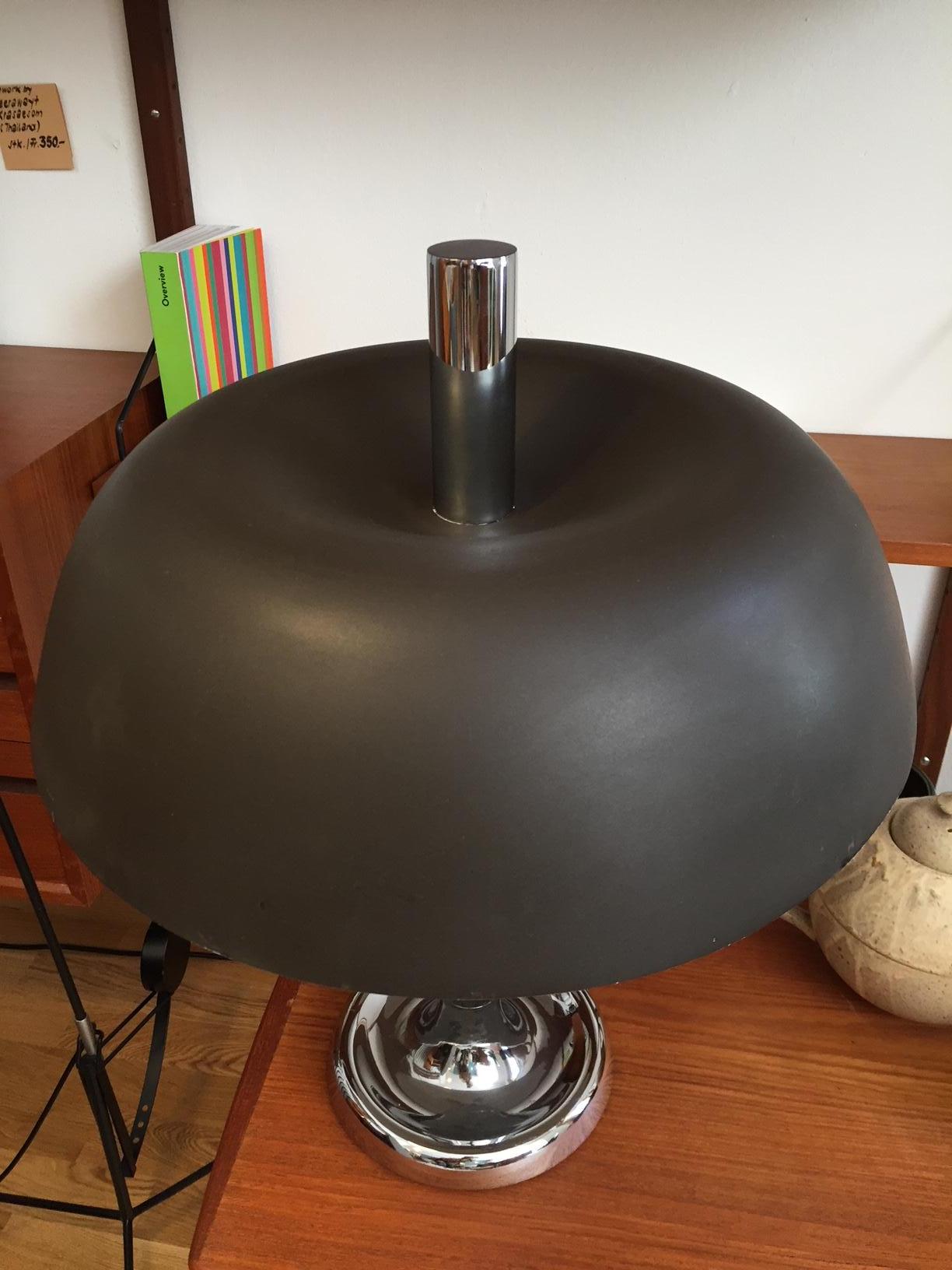 Midcentury mushroom table lamp was designed by Egon Hillebrand and produced by Hillebrand Lighting during the 1960s. The lamp features the distinctive characteristics of the Atomic Age. The black canopy shade, made of metal, is set on a chromed