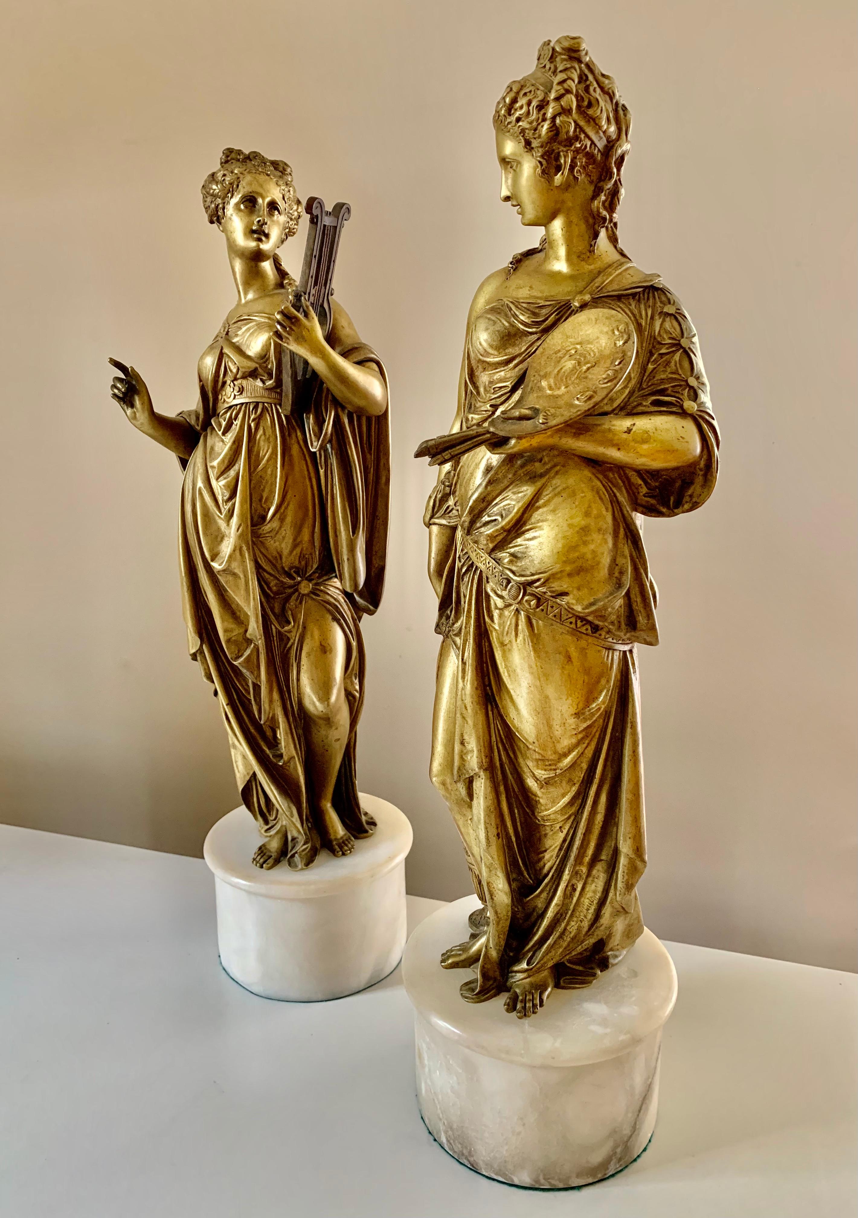 A pair of beautiful gilt bronze maidens representing Music and Art. 
Music holds a lyre, known for its use in Greek classical antiquity, in her left hand and is bringing her right hand forth to play the instrument with a beguiling expression. She