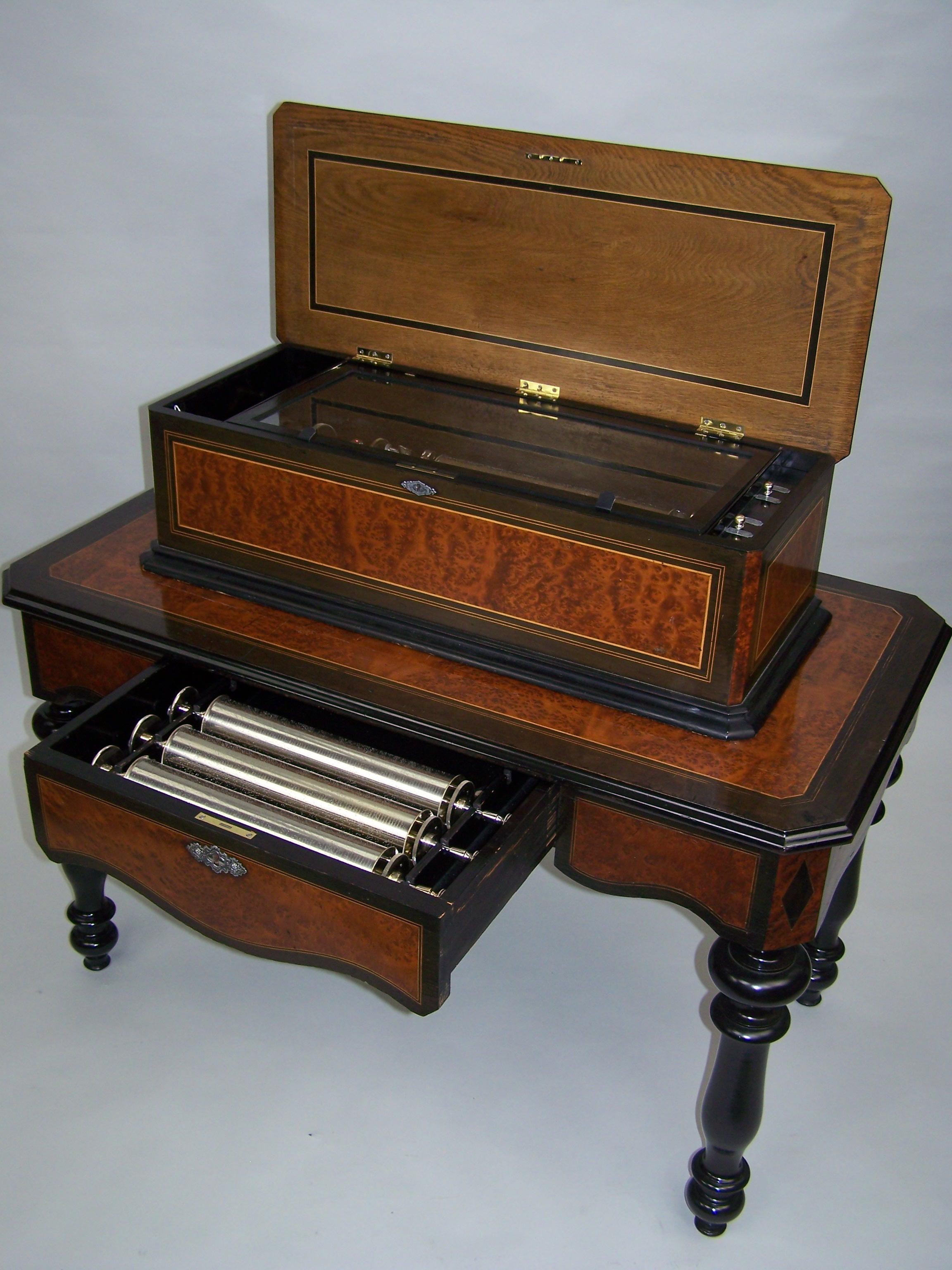 Rare cylinder music box. The 4 cylinders play 8 tunes as indicated on the original tunesheets.
The bird-eye marquetry of the case and matching table is all original. There are satinwood linings to top front, and all sides of the table. Opening the