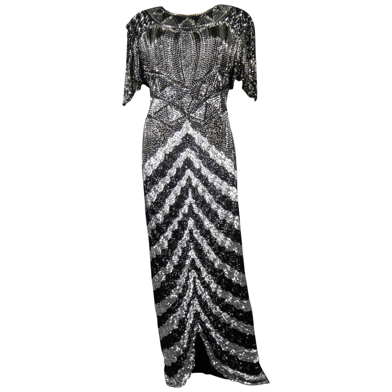Circa 1980/1985
France
Music-Hall Evening Dress inspired by Art Deco in Silver and embroidered with black and silver faceted paillons and silver tubular pearls from the 1980s. Skin-tight dress with short flounced sleeves with small shouder pads.