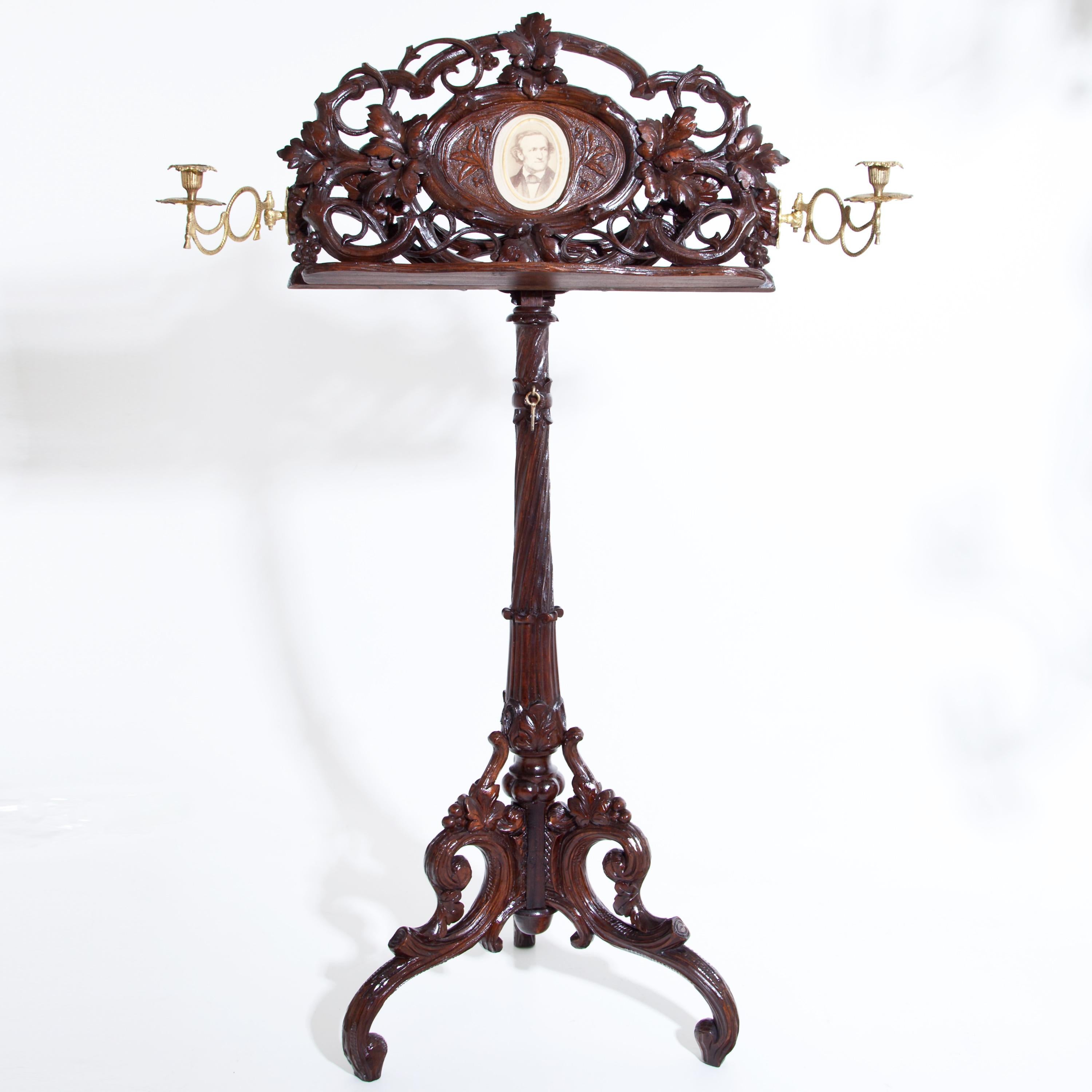 Music stand on a three-legged base made of walnut with rich carved vine and grape decoration and a central medallion with a portrait of Richard Wagner, flanked by two gilt candlesticks.
