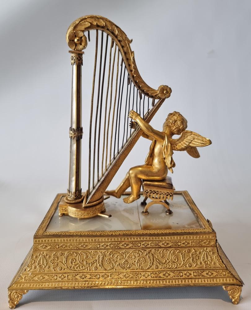 A fine, early and very unusual Palais Royal Cupid and Harp musical box
with two-air cylinder movement. The finely modelled cupid sits upon an Empire stool and plays a classical 16 string harp with acanthus leaf scroll top arm. The front tapering
