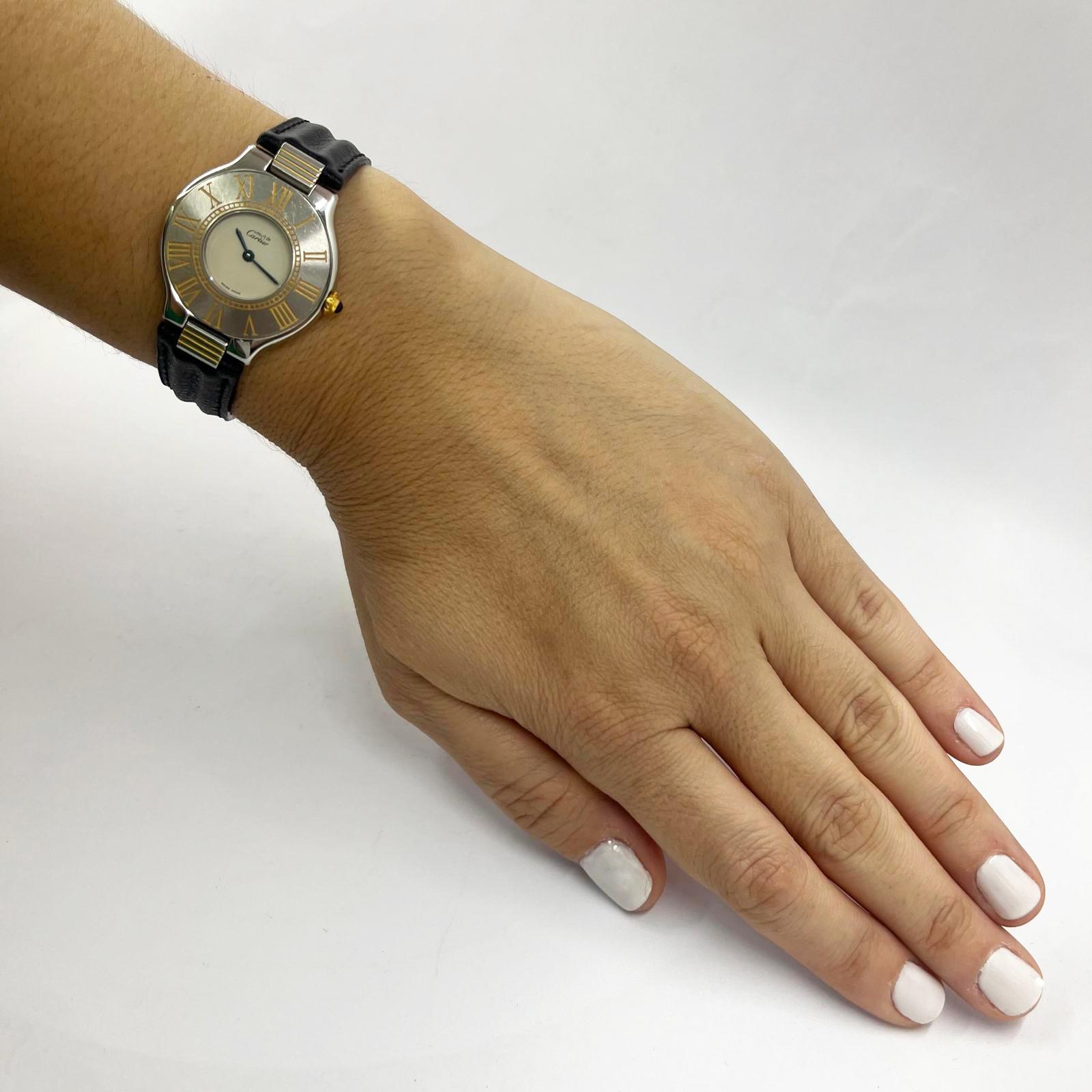 Reloj de cuarzo Must de Cartier 21 de acero inoxidable con corona y detalles en el bisel de oro amarillo. Caja de 31 mm con correa original de piel de becerro negra con hebilla desplegable Cartier.